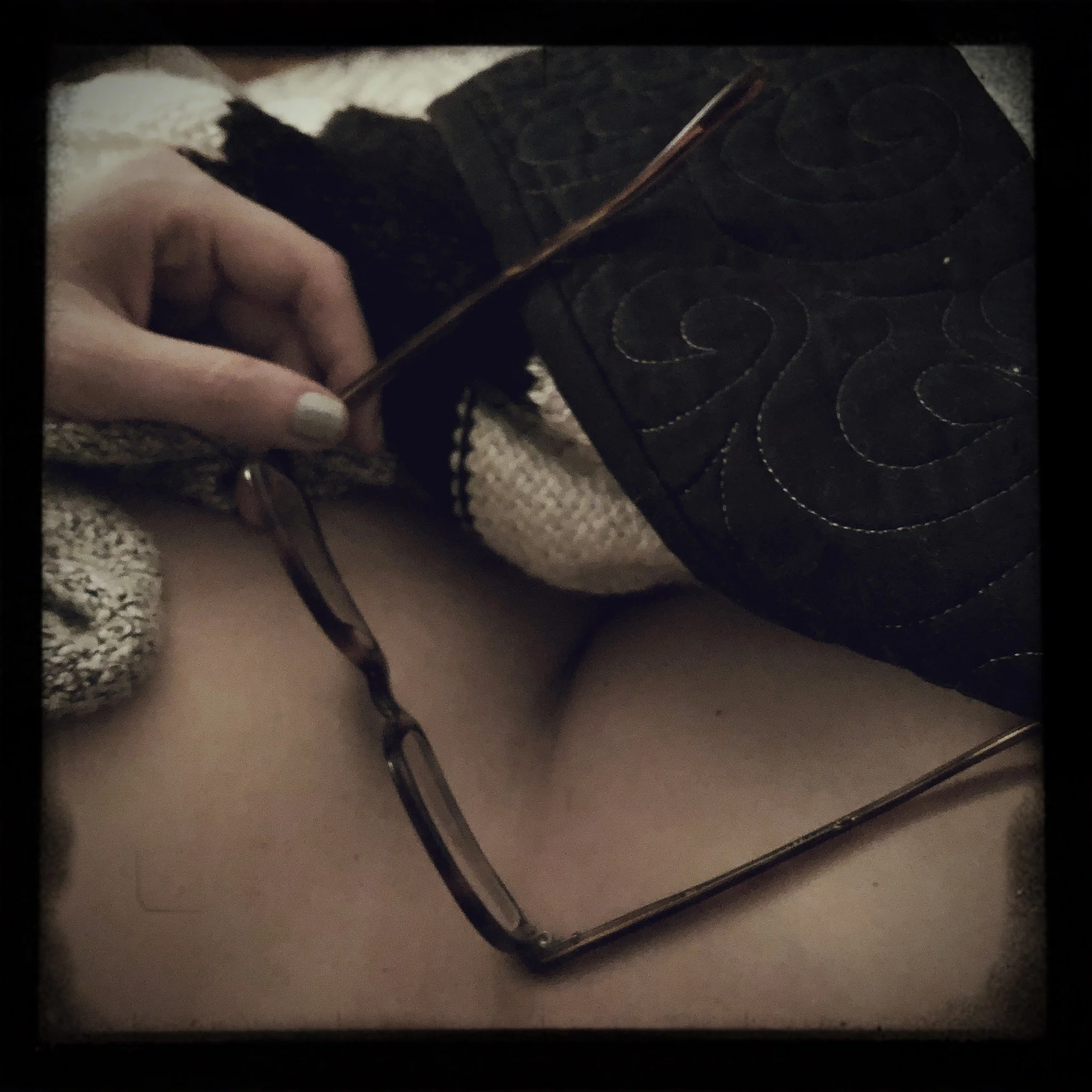 Close-up of a hand holding a pair of glasses, with a mirror reflecting a person's midsection and a patterned fabric garment.