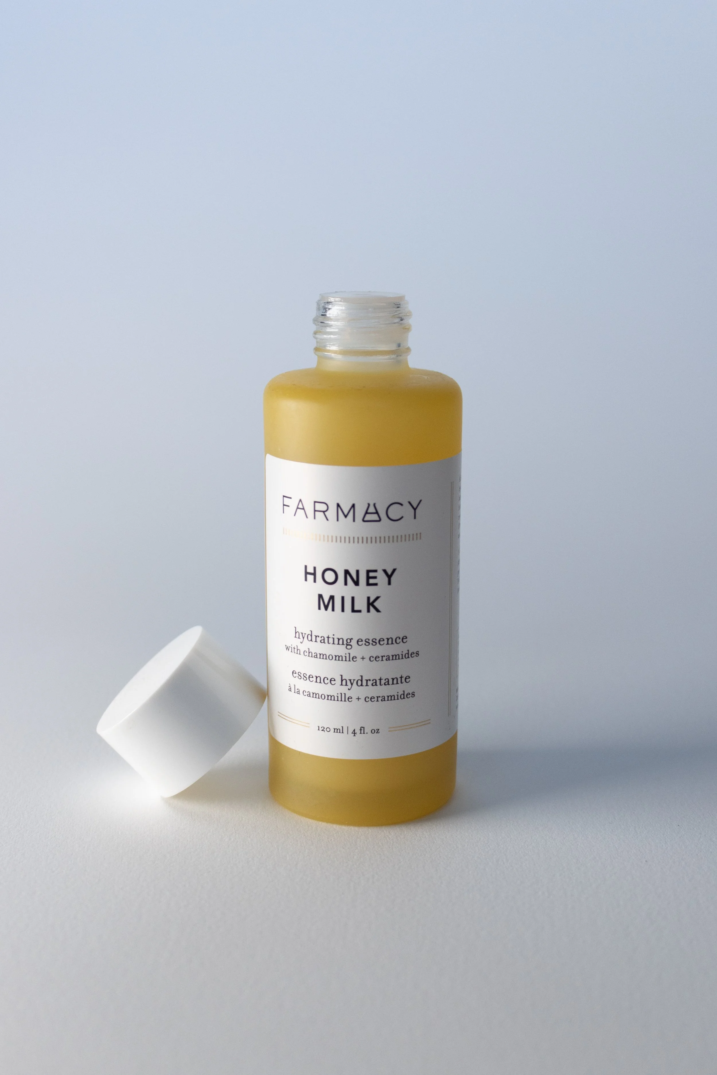 Farmacy Honey Milk Toner front. A yellow bottle with a white label and white cap off leaning against the left side of the bottle