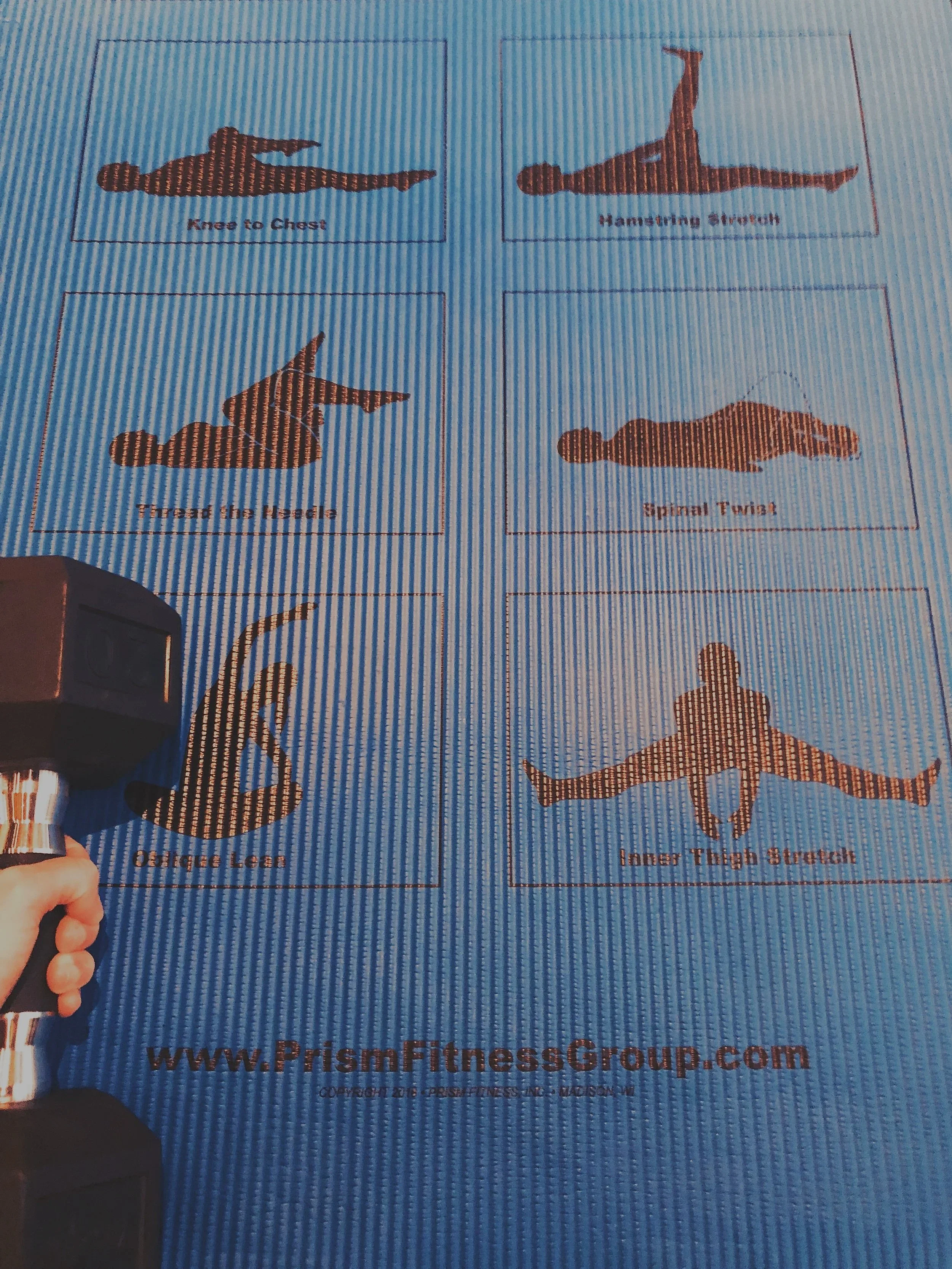 Printed exercise instructions with silhouettes of different yoga poses, including 'Knees to Chest,' 'Hamstring Stretch,' 'Tread the Hurdle,' 'Spinal Twist,' 'Oblique Lift,' and 'Inner Thigh Stretch.' A person's hand holding a handheld scanner is pointing at the exercise instructions.