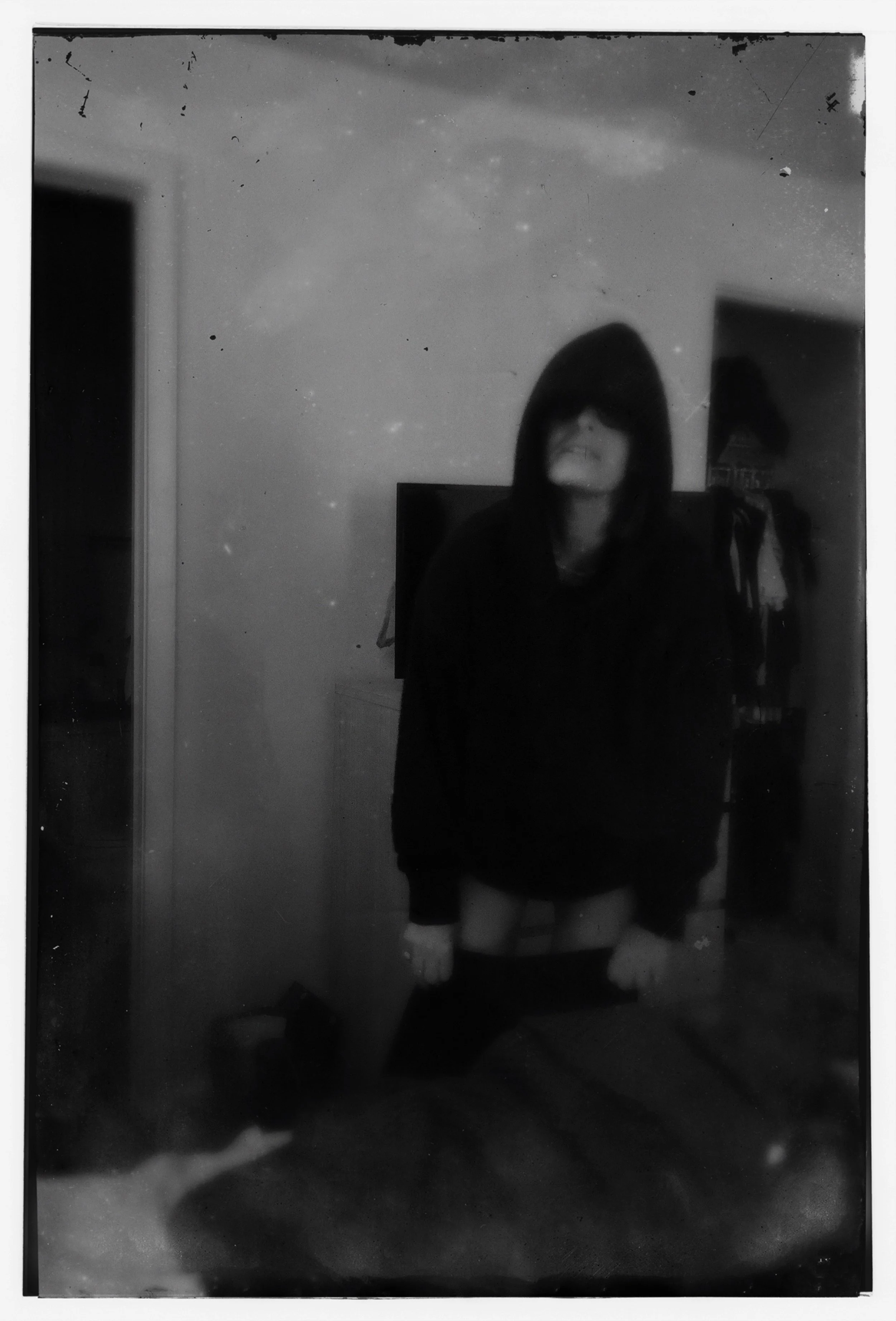 A person standing in front of a mirror, wearing a hooded jacket and stockings, with a smile showing teeth, getting dressed.