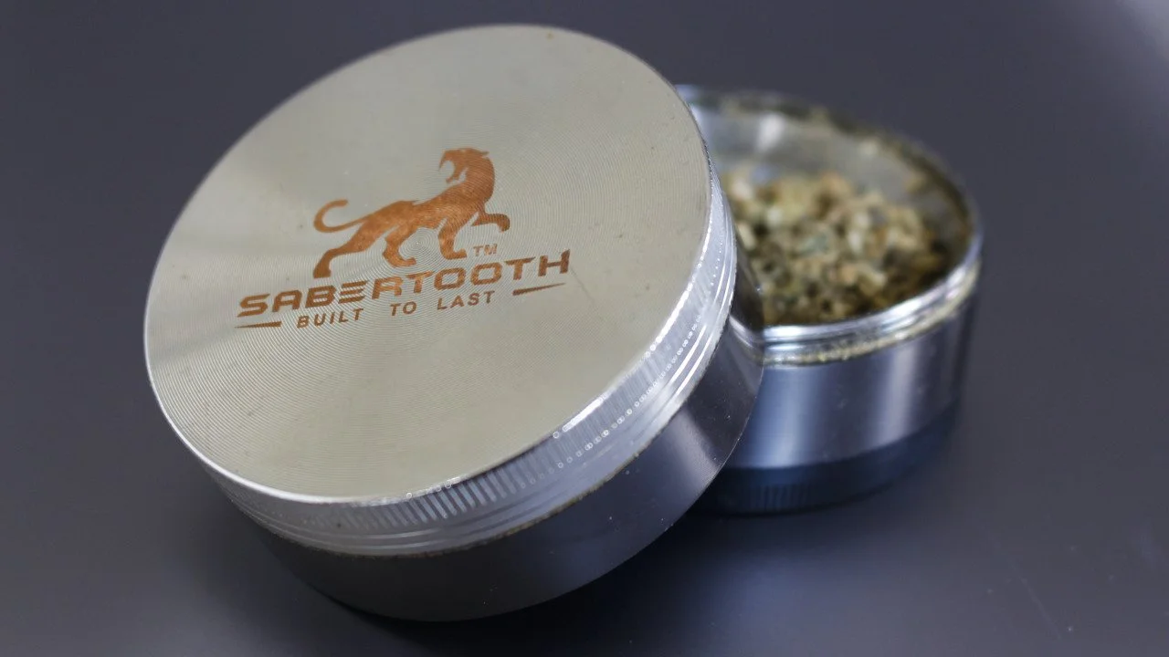 A grinder filled with flower and with an image of a sabertooth tiger and decorative words