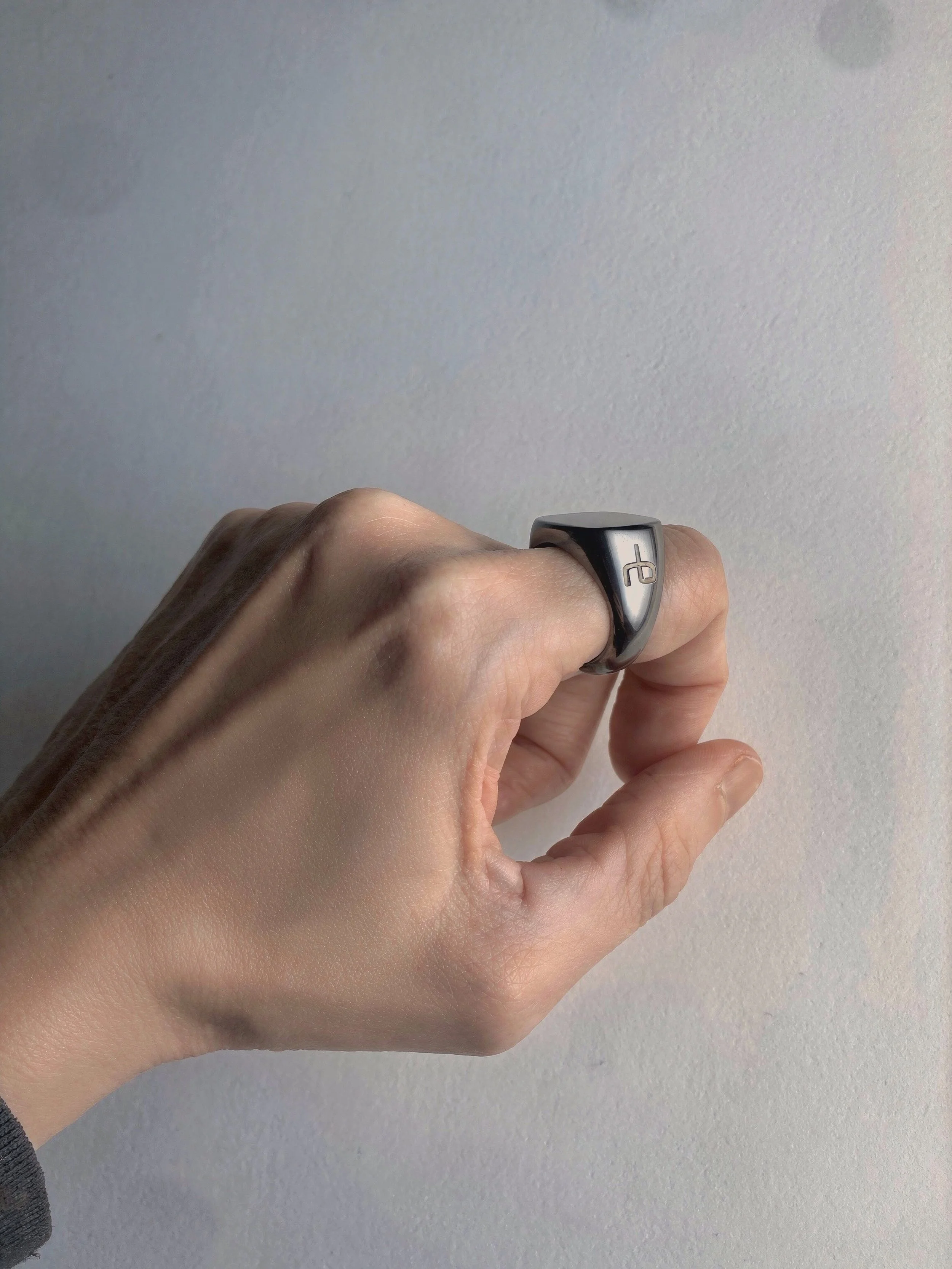 Hand shown from the right with a large titanium signet ring from Rag and Bone on the first finger.