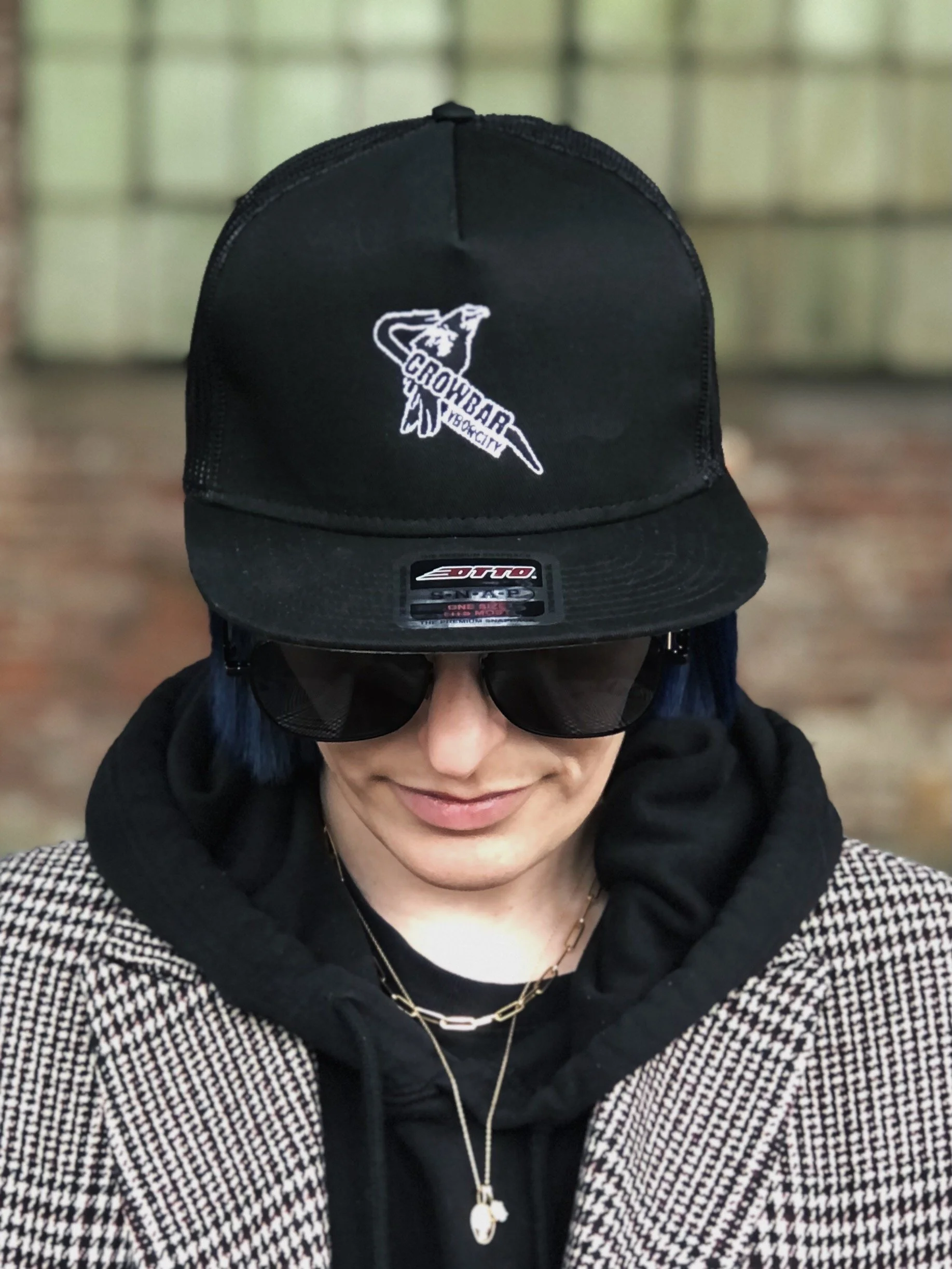 Woman with a baseball hat, dark sunglasses and a hoodie with a tweed coat.