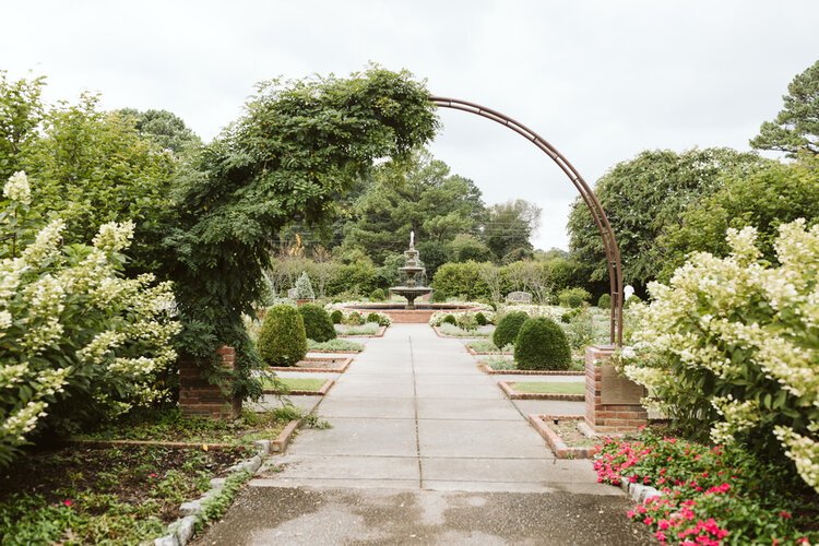 Garden pathway with archway, greenery, and fountain