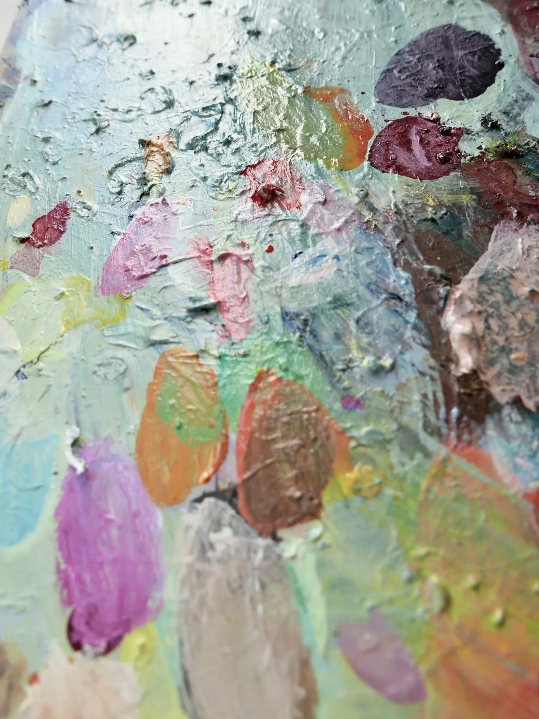 Close-up view of an artist's palette with thick, textured oil paint in various colors, including pink, orange, brown, purple, green, and white.