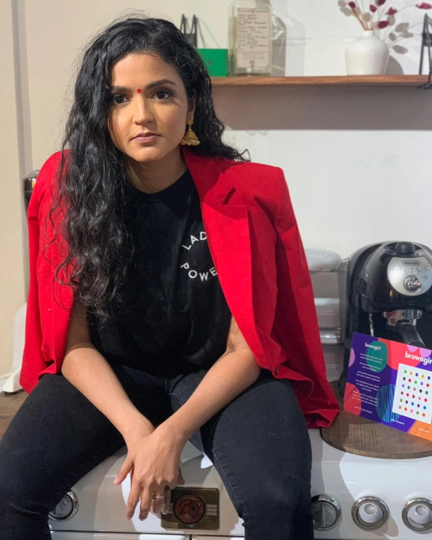 woman-of-color-with-curly-black-hair-wearing-black-outfit-and-red-blazer
