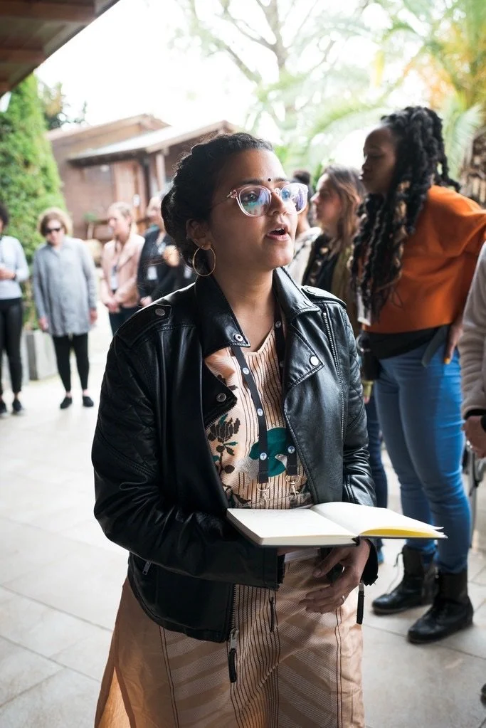 Deepti Sharma speaking at an outdoor event in New York City, holding a notebook