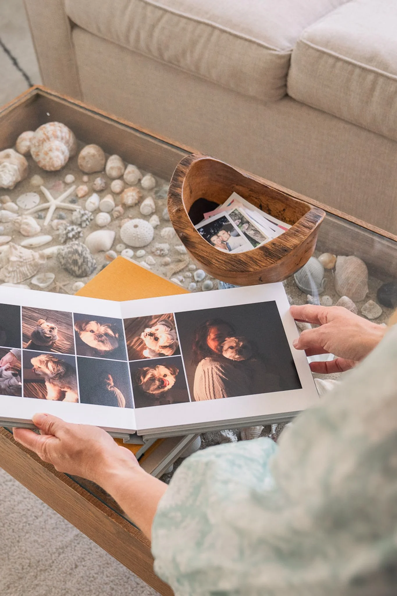 Over the shoulder shot of a woman holding open a beautiful heirloom photo album on a beachy-aesthetic coffee table