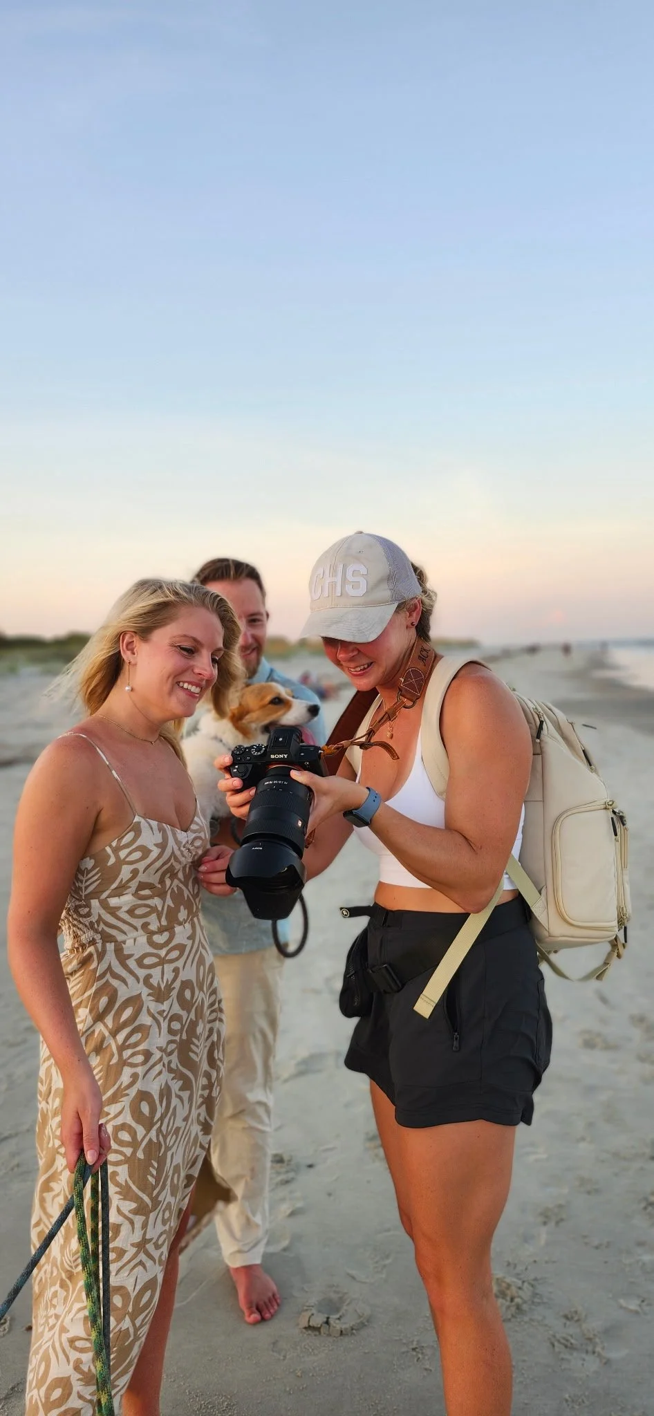 Behind the scenes of professional pet photography on Folly Beach, photographer Amy is showing images in camera to her clients, a young couple with three corgis