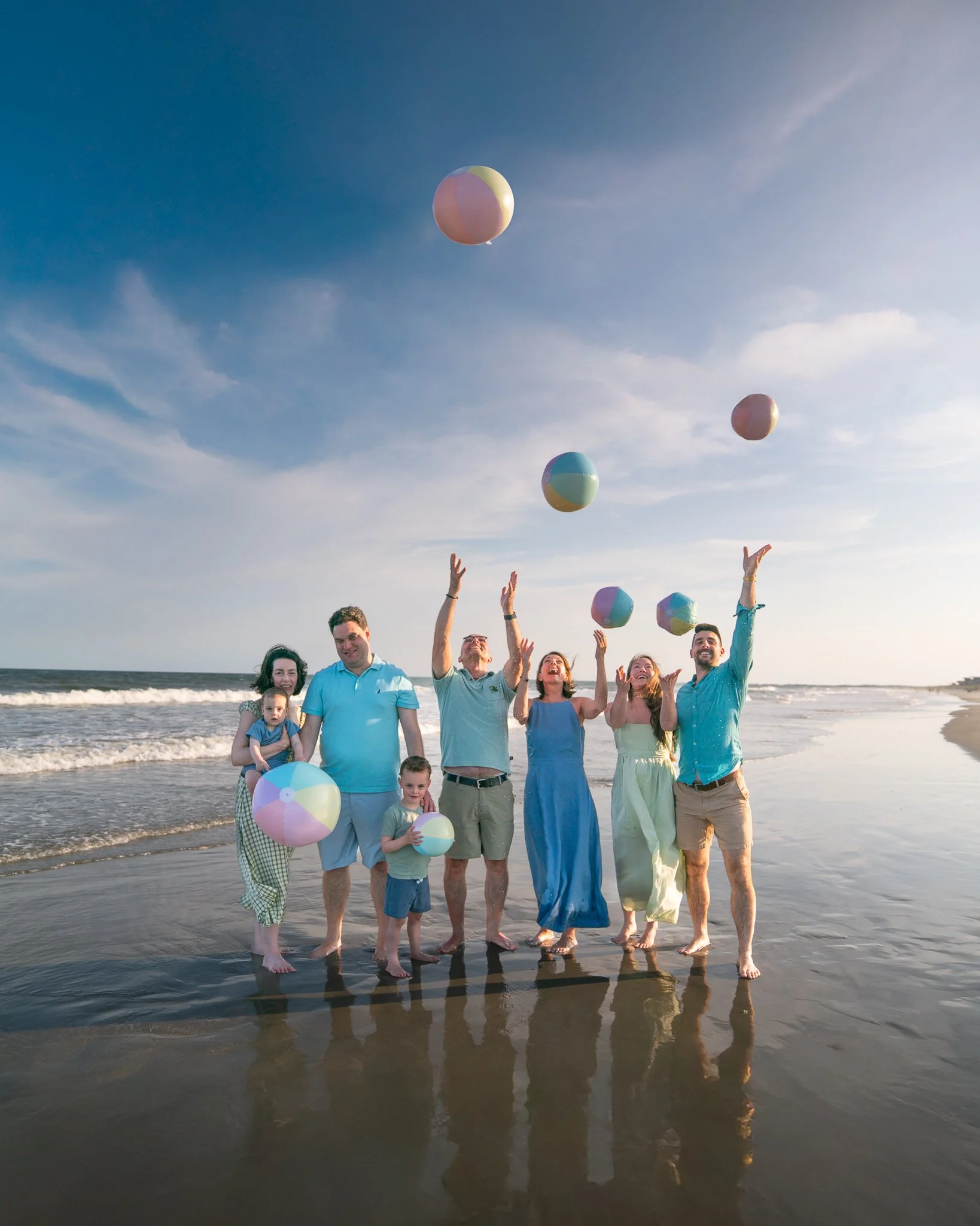 A large group smiles and throws beach balls up in the air on their Folly Beach family vacation