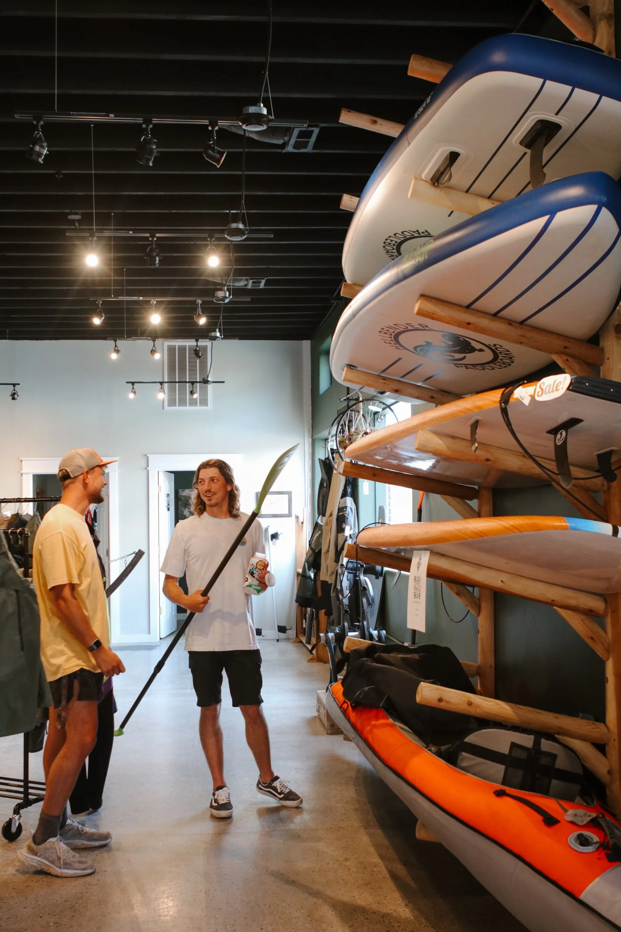 Two men talking in a store with paddleboards and kayaks on display.
