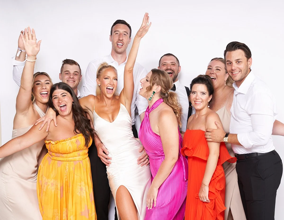 Group of people dressed in formal attire smiling and celebrating together against a white background.