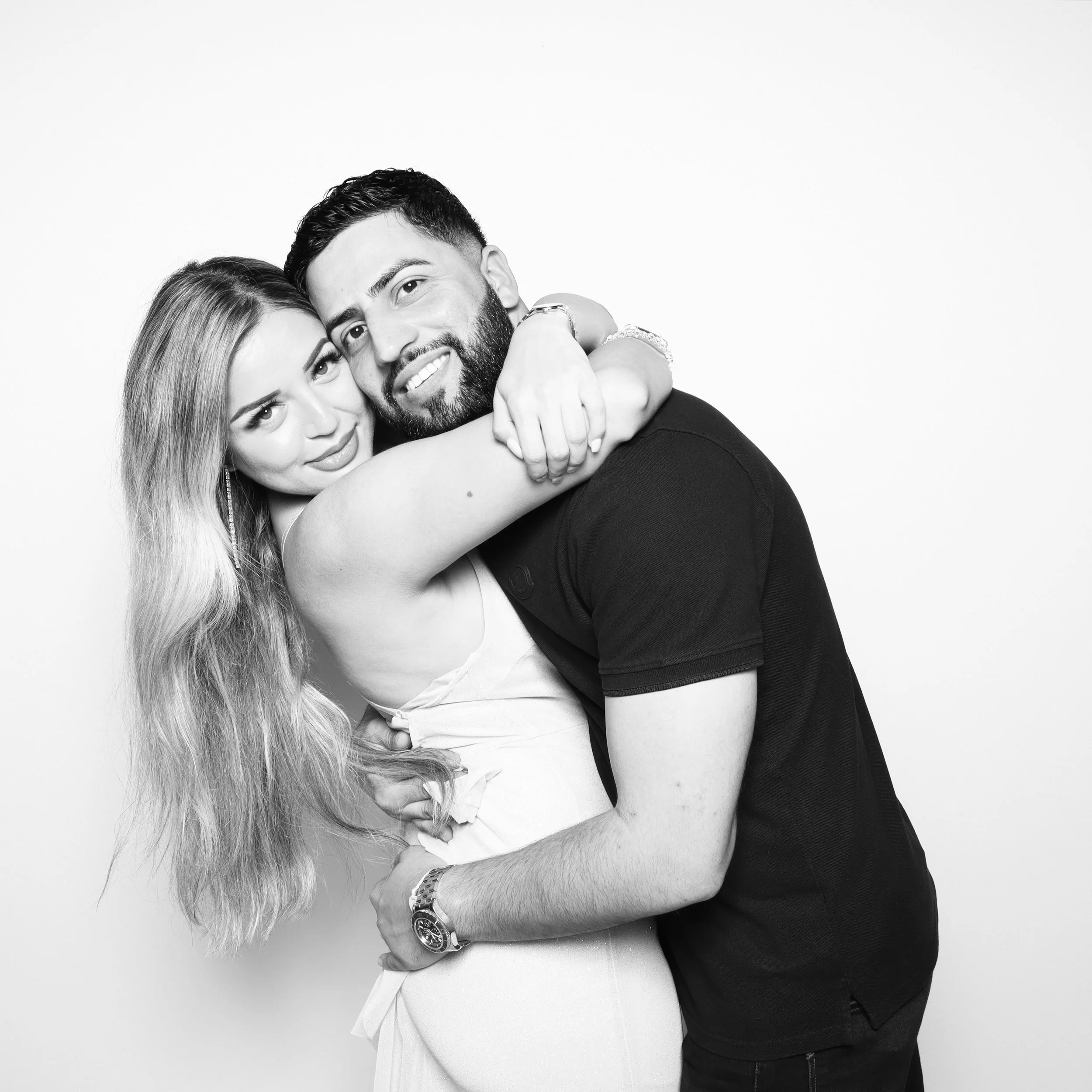 Black and white photo of a happy couple embracing each other, with the woman on the left and the man on the right, smiling at the camera.