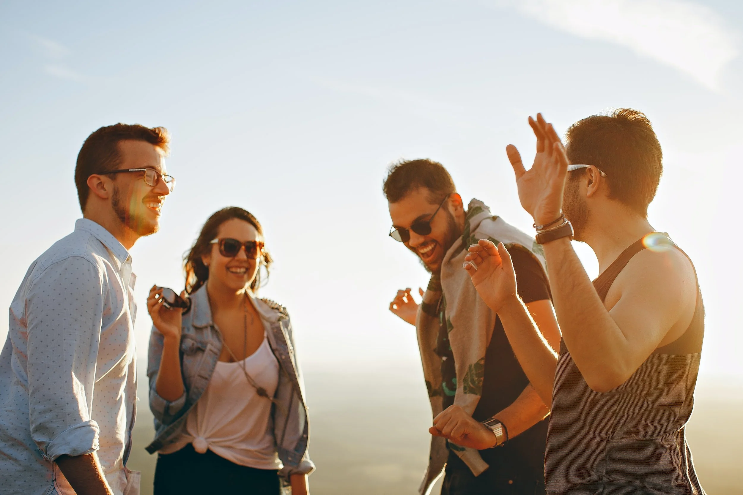 Four young adults laughing and enjoying each other's company outdoors during sunset.