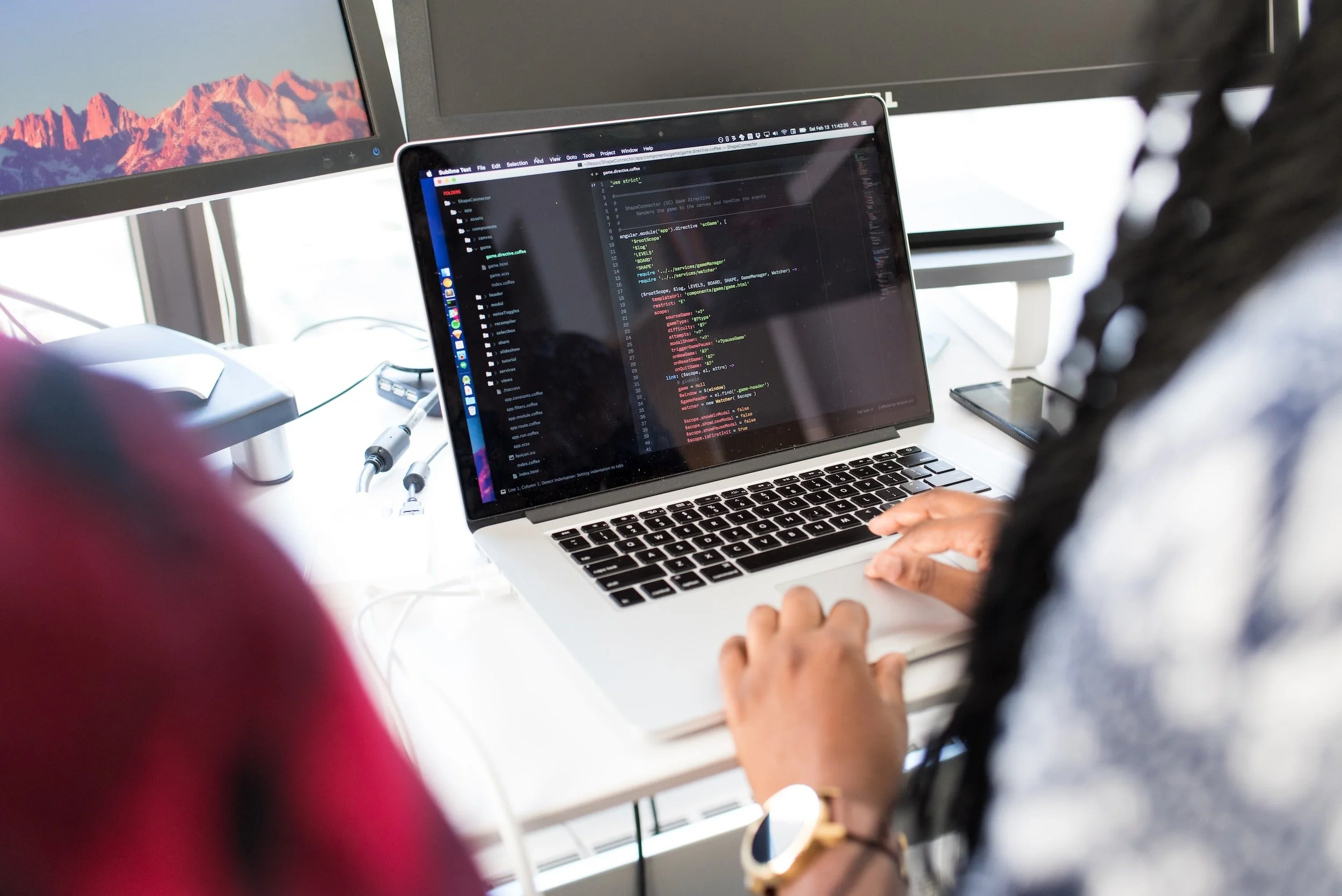 People working on a laptop with code visible on the screen in an office setting.