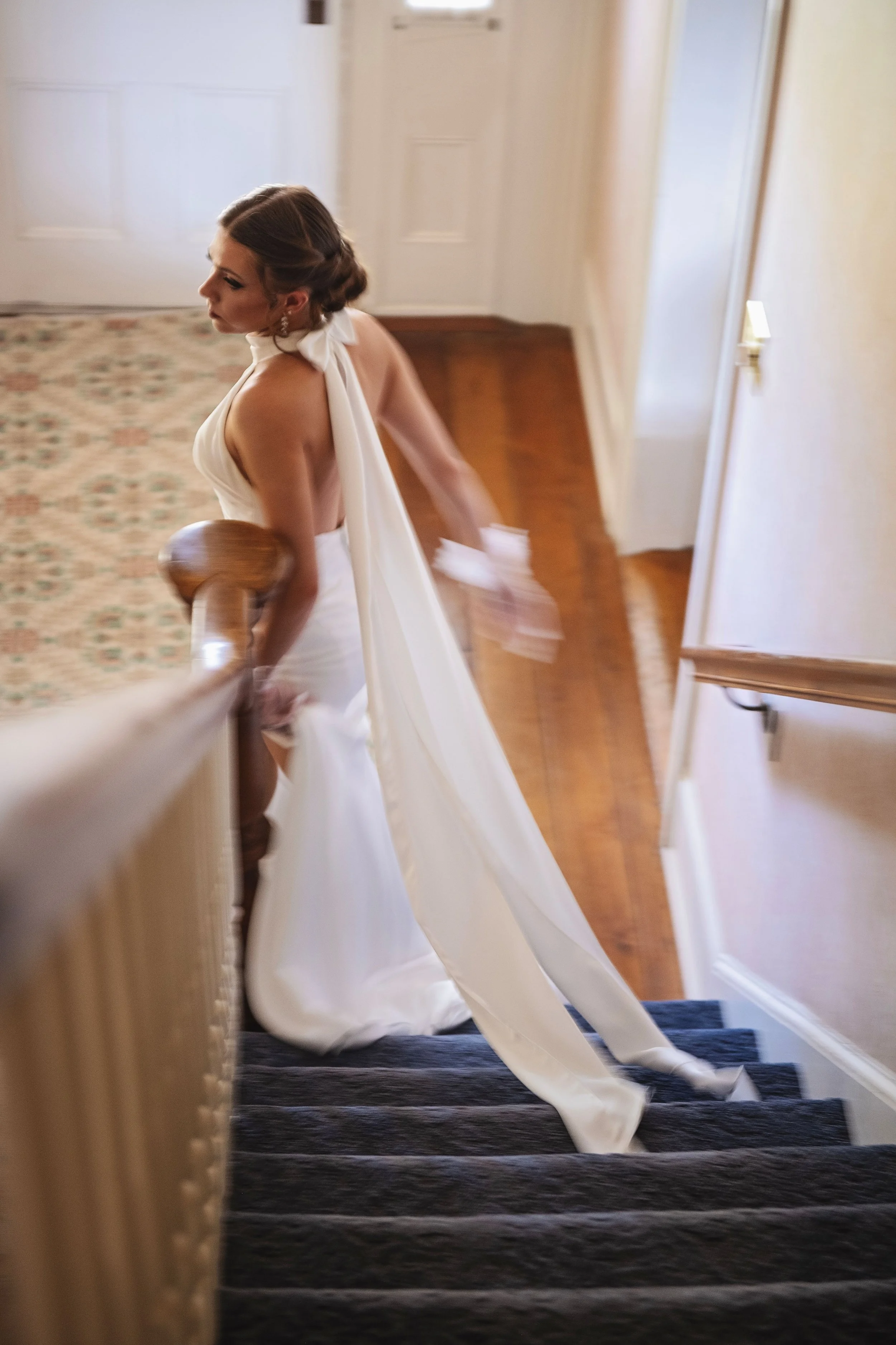 A woman in a wedding dress walking up a staircase with a wooden handrail.