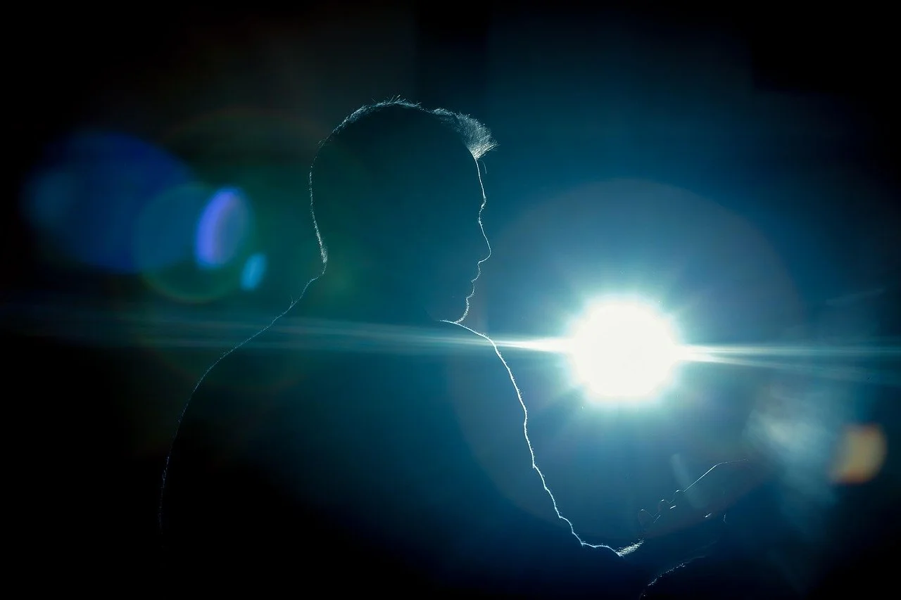 Silhouette of a person looking at a phone with a bright light behind them creating a lens flare effect.