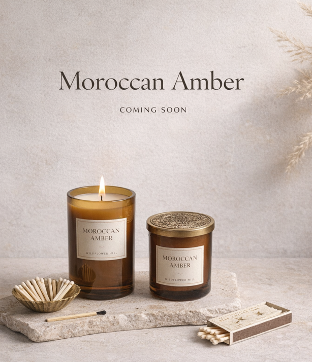 Image of two candles labeled Moroccan Amber, a bowl of matches, and a box of matches on a stone slab with a neutral background.