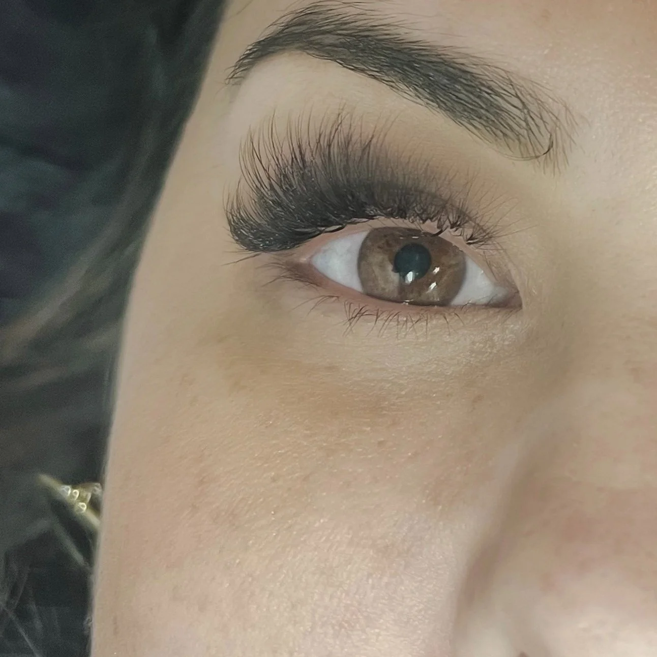 Close-up of a woman's eye with brown iris, makeup, and long eyelashes.