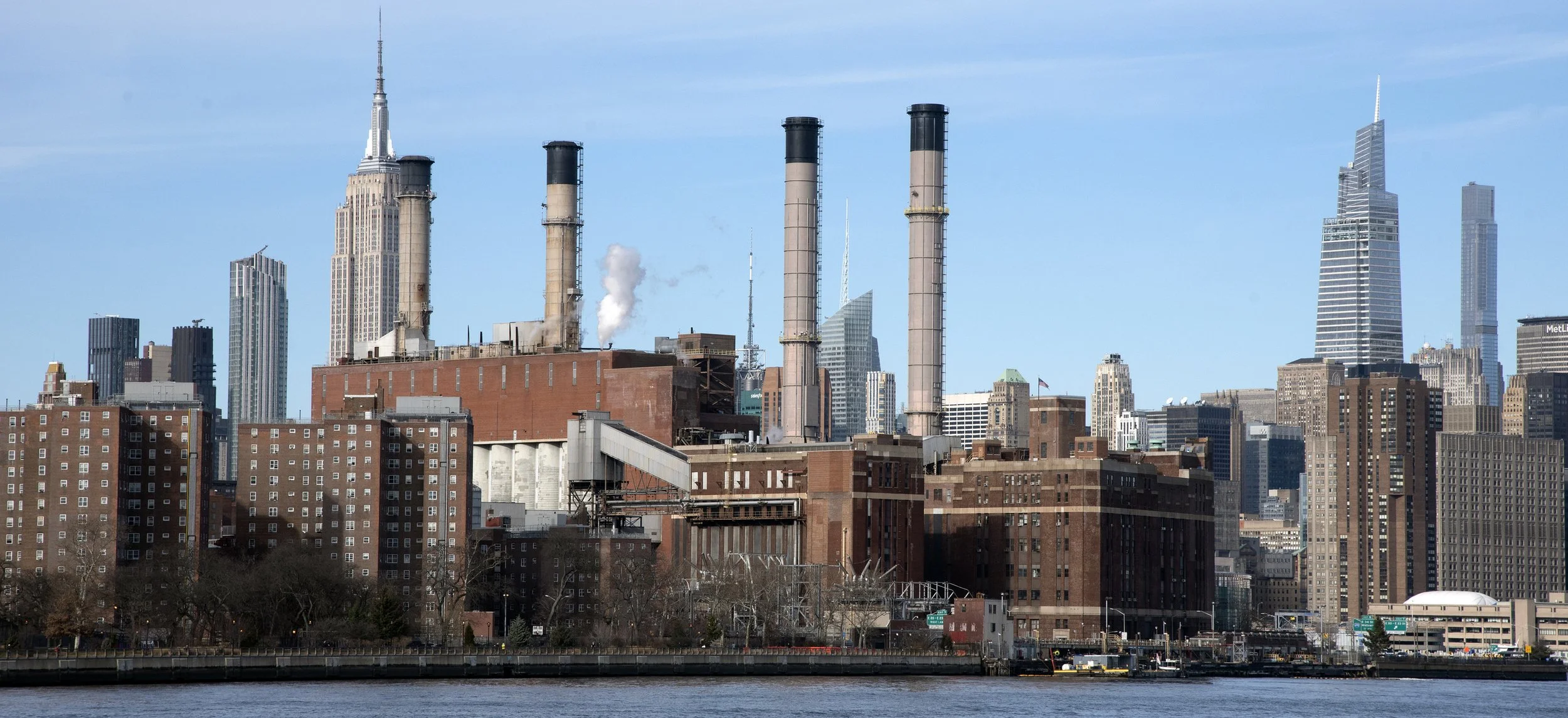 A view of the Manhattan skyline from the East River in New York City, showing Con Edison industrial buildings in front of the Empire State Building and skyline.