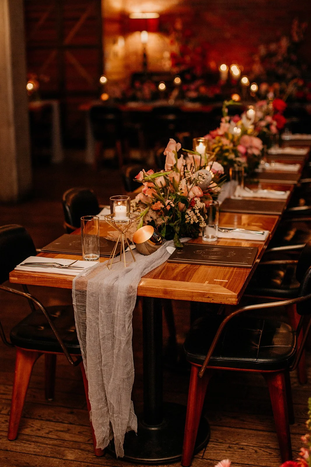long wooden table with table runner, colourful flowers and candles inside Chambar Restaurant