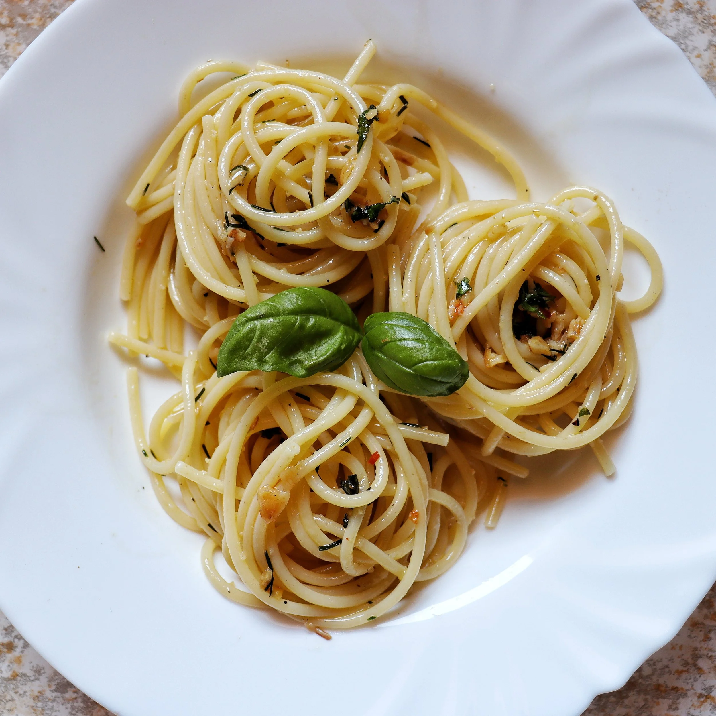 Plate of aglio e olio, garnished with fresh basil leaves.