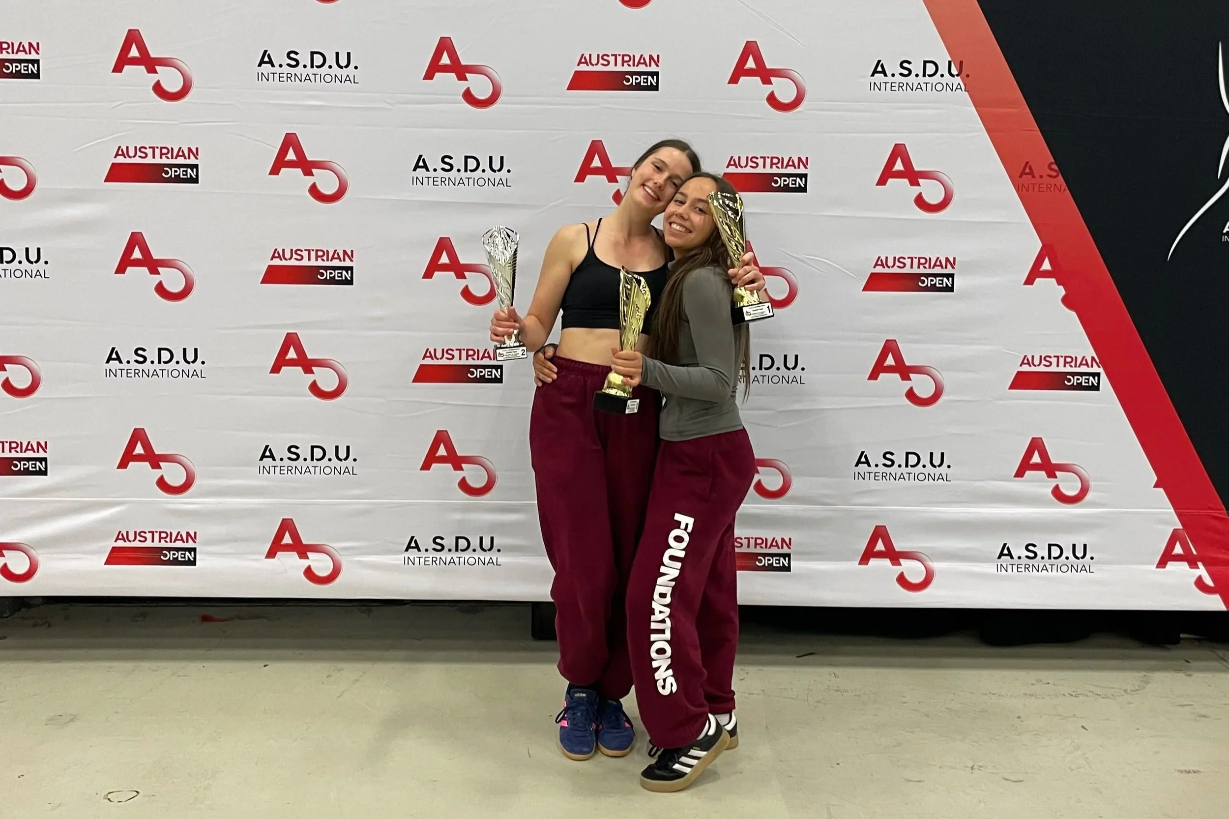 Christina Muntean und Chiara Adler stehen nebeneinander auf der Bühne der Austrian Open und halten stolz ihre Trophäen in den Händen. Beide strahlen vor Freude und Erfolg, während sie ihren gemeinsamen Moment feiern.