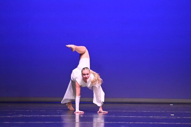 Eine Tänzerin macht eine Handstand-Pose auf der Bühne vor einem blauen Hintergrund.
