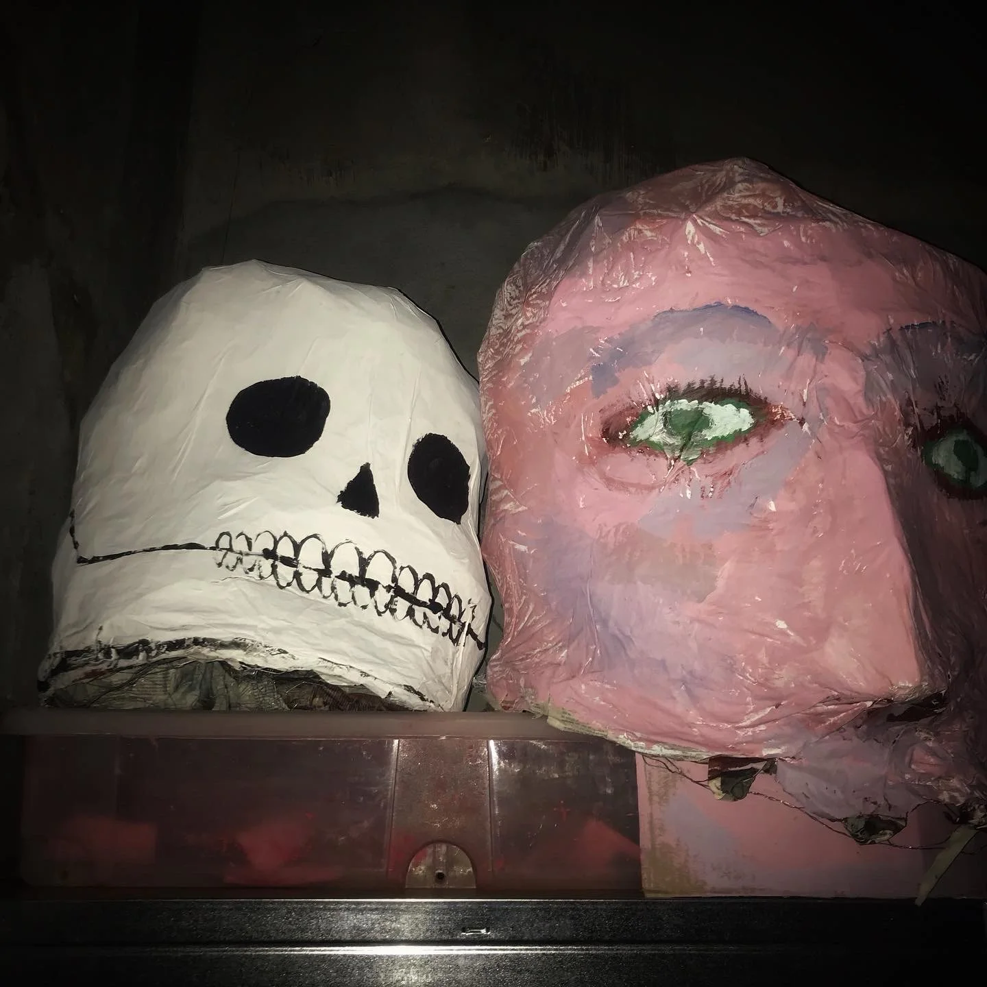 Deux sculptures de masques, un squelette et un visage humain, fabriquées avec du papier ou du papier mâché, dans un style artistique.