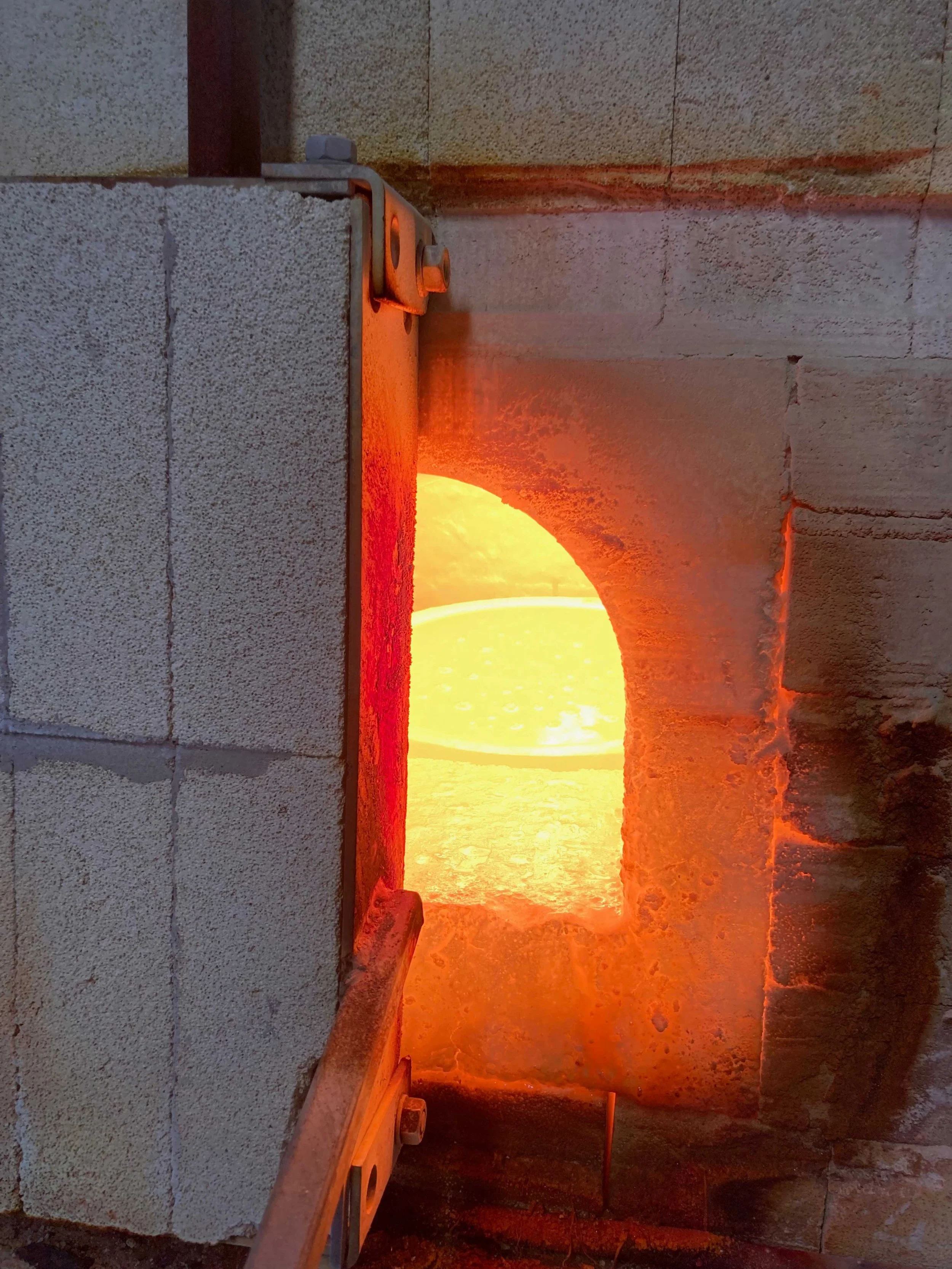 A view of a pizza oven with a glowing fire inside, seen through an arched opening in the brick structure.