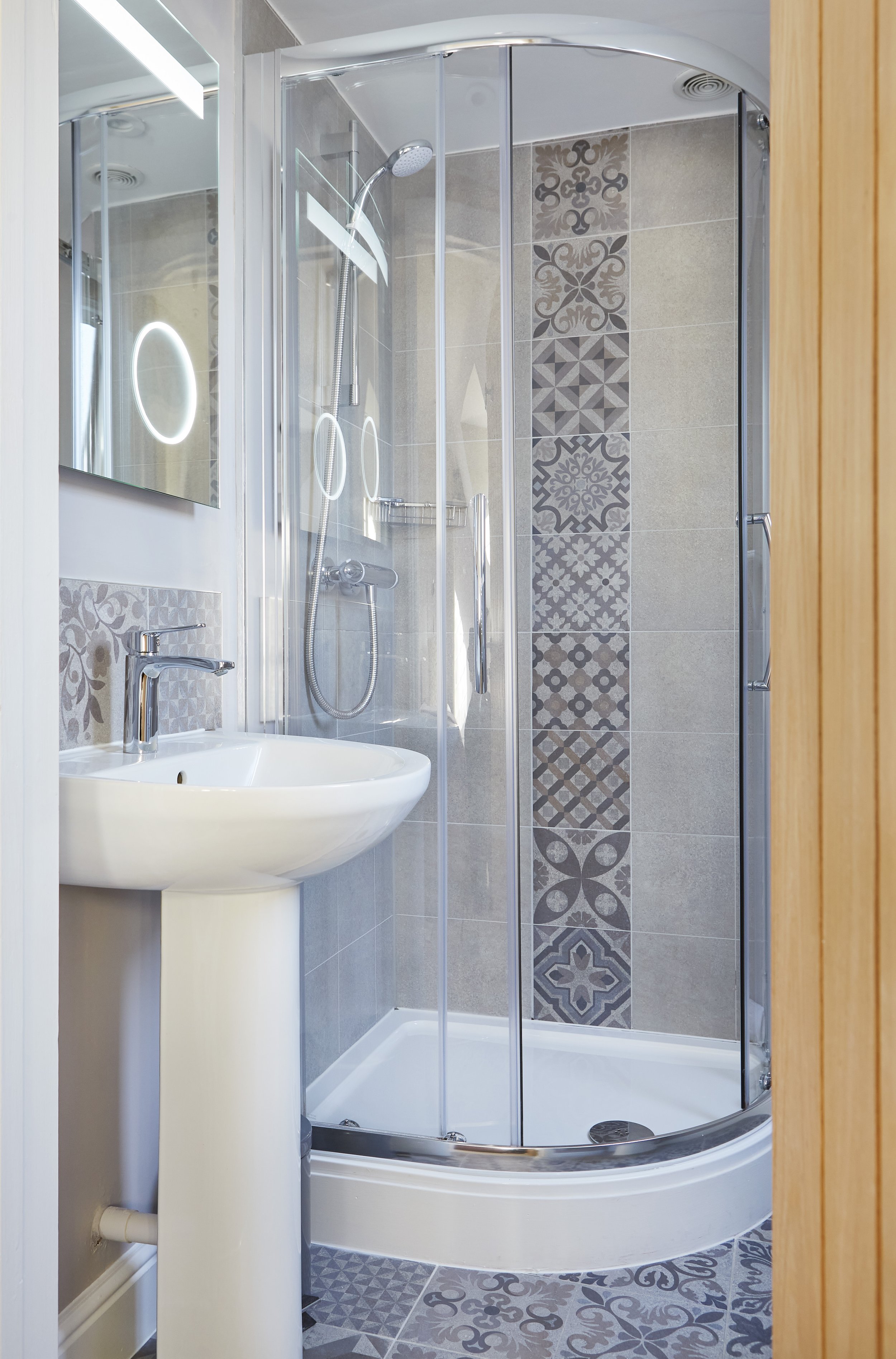 Modern bathroom with a corner shower enclosure, patterned tiles, and a pedestal sink.