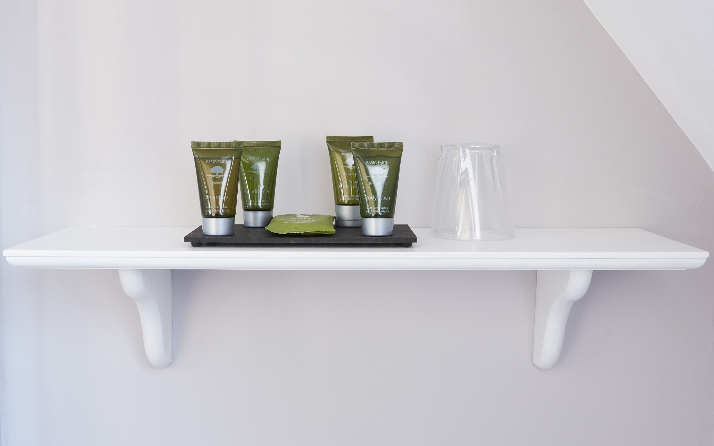 Bathroom shelf with toiletries and an upside-down glass on a white wall.