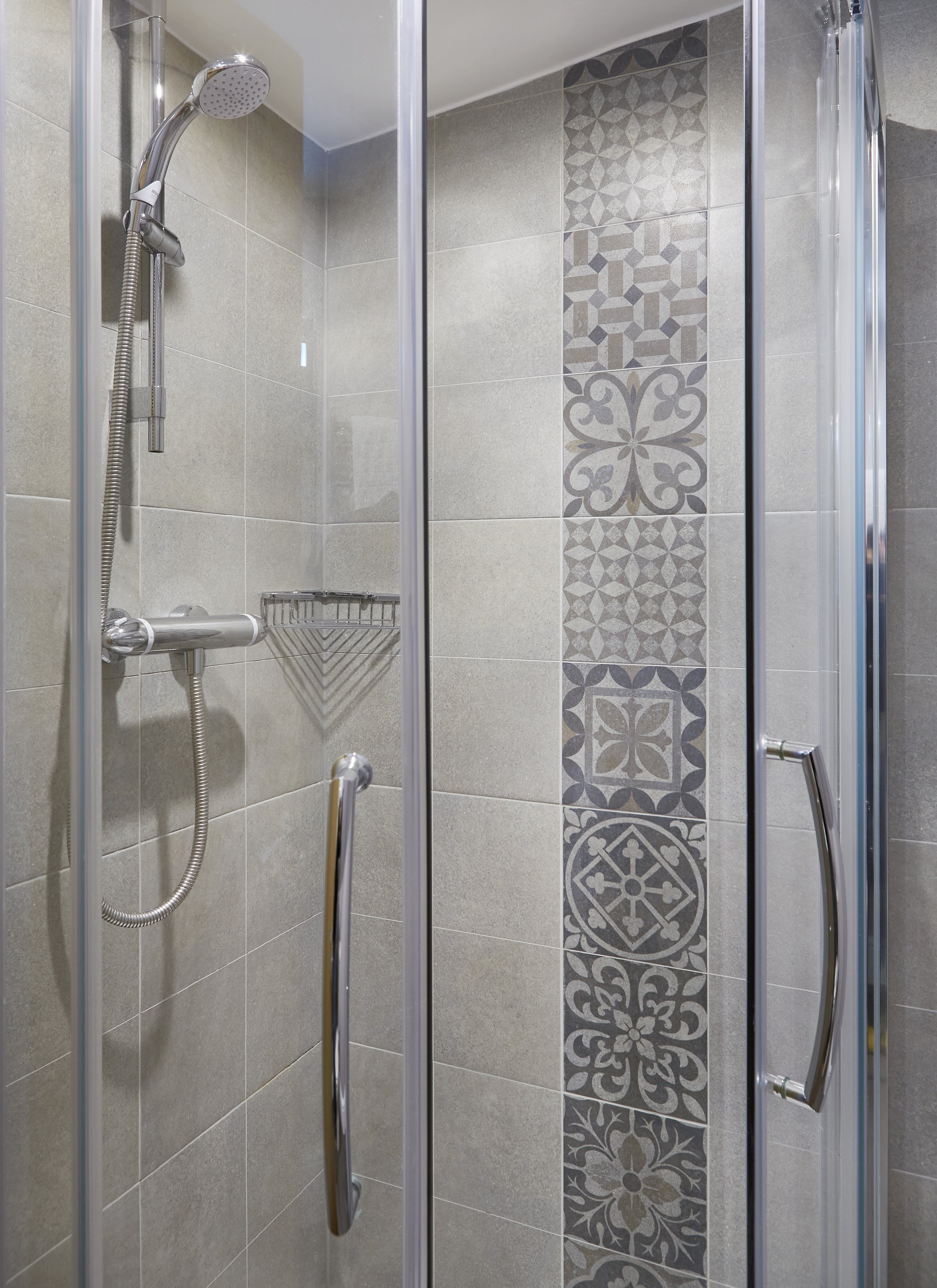 Modern shower enclosure with decorative tiles, handheld showerhead, and chrome fixtures.