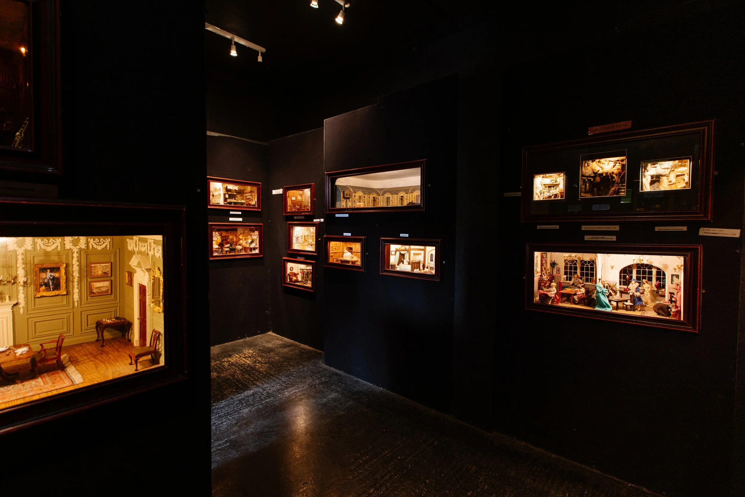 Exhibit of miniature room dioramas displayed in a dimly lit gallery.