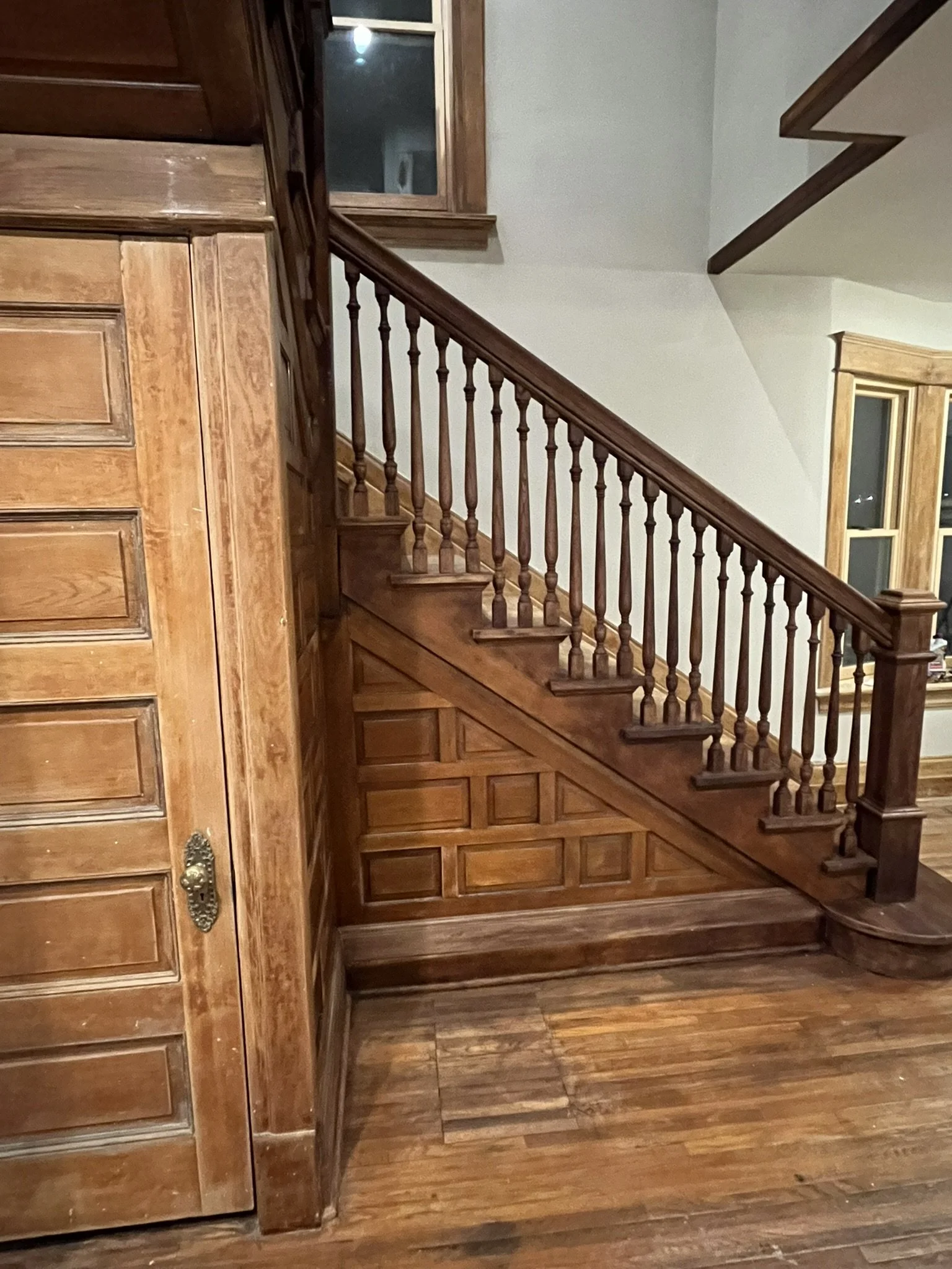 Interior view of a staircase with a wooden handrail and balusters, and wood-paneled walls and flooring.