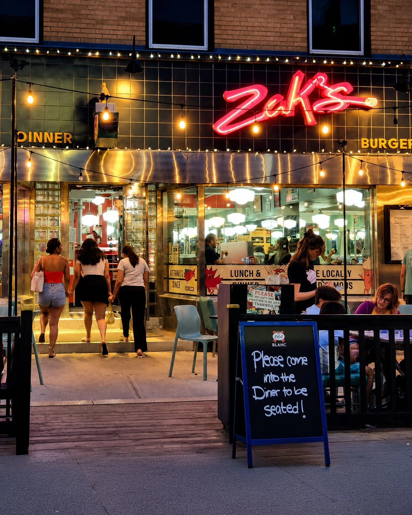 Summer nights hit different under the Zak's glow. ✨🍔 The string lights are on, the booths are filling up, and the grill's going strong. Late dinner, a milkshake run, or just a nowhere-else-to-be kind of night &mdash; there's always a booth with your