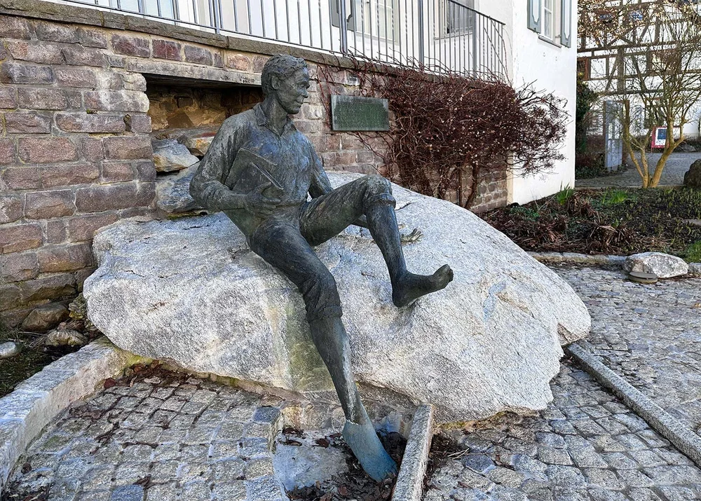 Der junge Sebastian Kneipp sitzt am Marktplatz von Bad Grönenbach auf einem Stein.