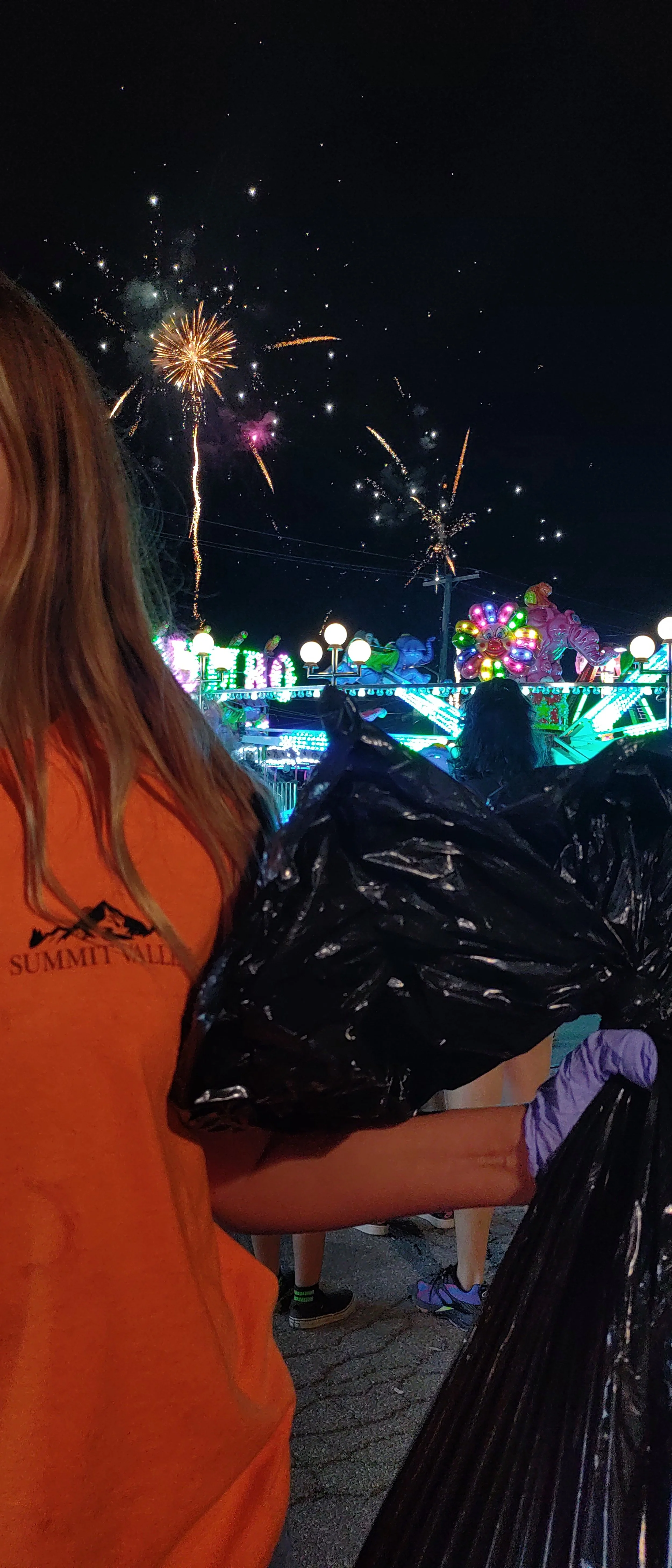 Large crowd attending an outdoor concert or festival with colorful smoke effects and a stage with bright lights and digital screens.