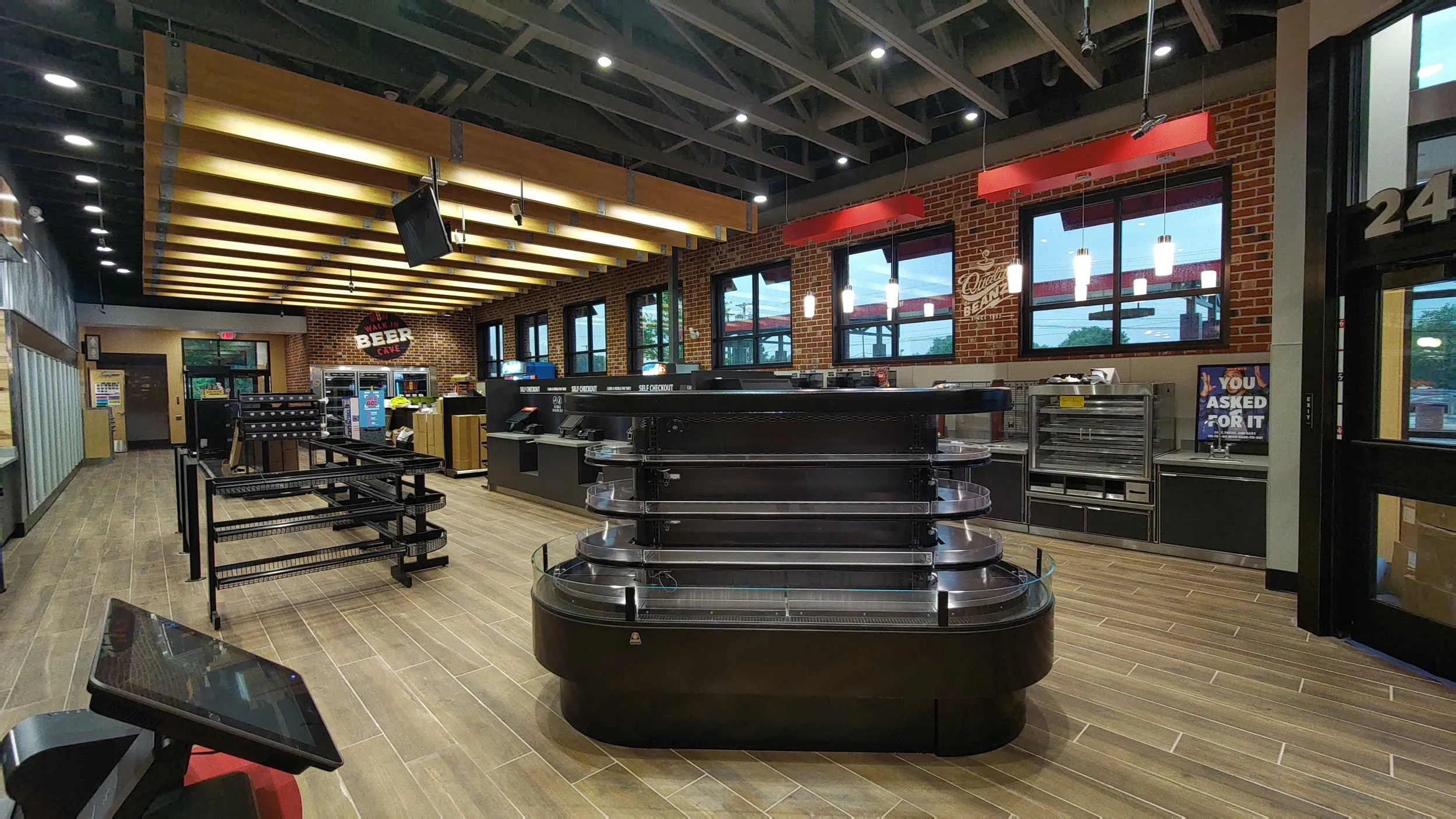 Empty convenience store with a black checkout counter in the center, brick walls, large windows, and hanging lights.