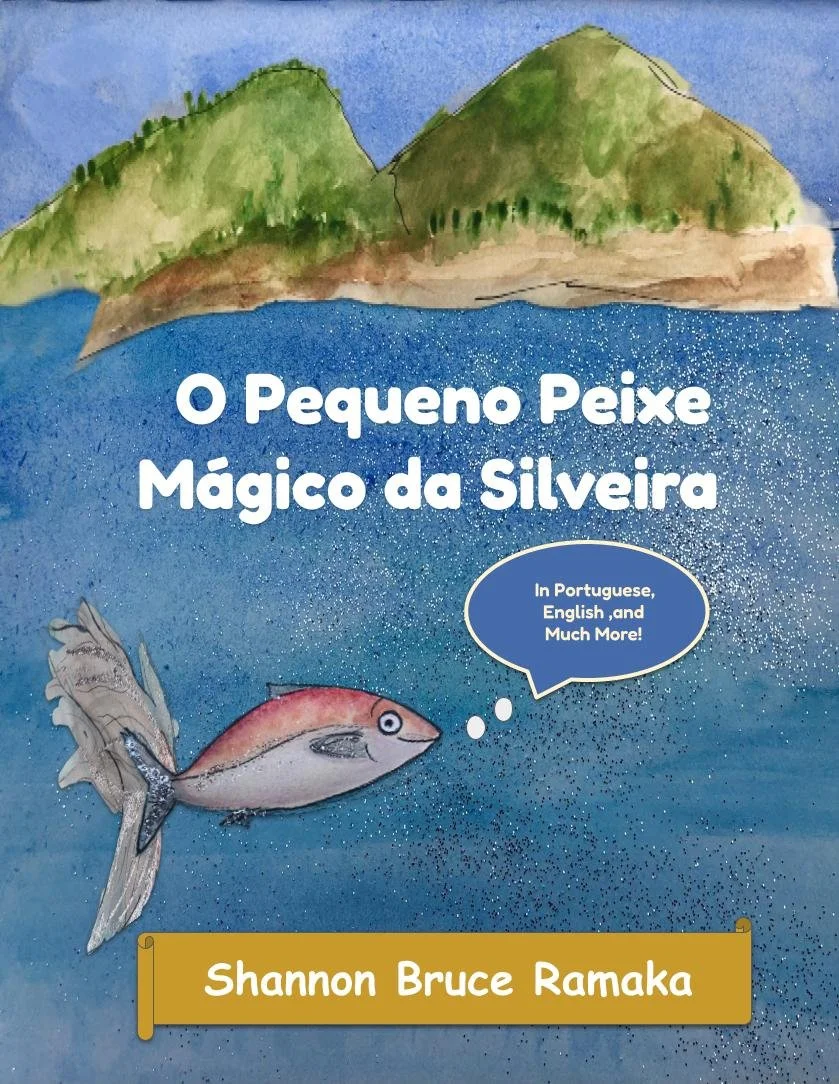 Book cover titled "O Pequeno Peixe Mágico da Silveira" by Shannon Bruce Ramaka. The cover features a colorful illustration of a fish with a boat and green island hills in the background. The fish has a speech bubble that says, "In Portuguese, English, and Much More!" The background of the cover is blue with white speckles, resembling water.