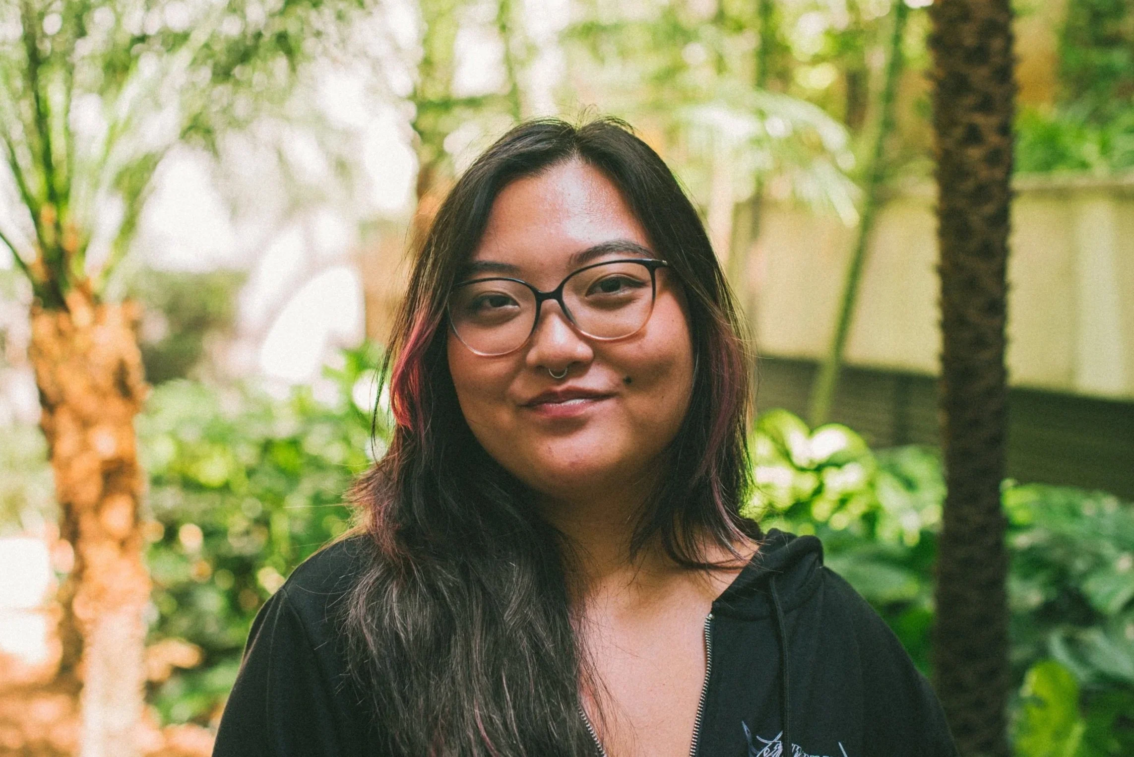 Fotografia de Karina, uma mulher adulta jovem, de descendência japonesa, de cabelo escuro médio, liso. Ela usa óculos de grau e veste um blazer branco com camiseta preta.
