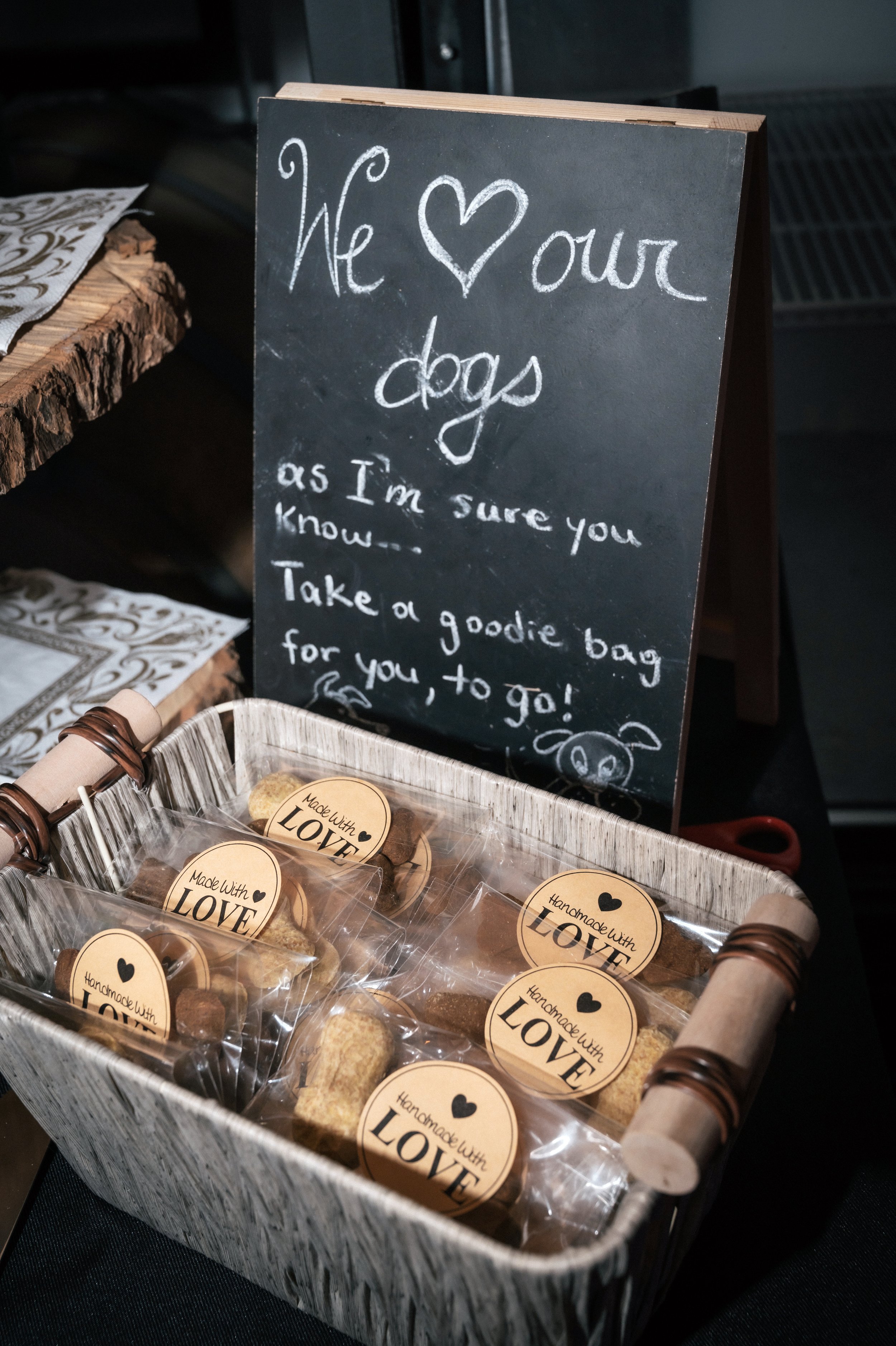 A basket of individually wrapped dog treats labeled 'Made With LOVE' and a chalkboard sign with a dog-themed message about caring for dogs.