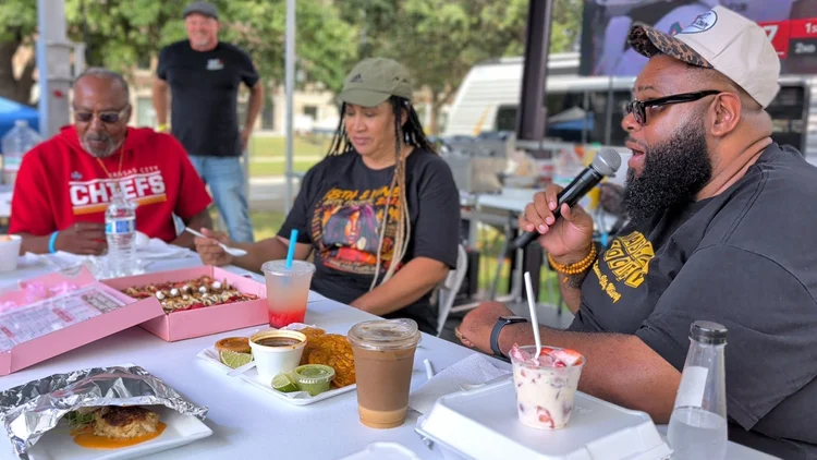 People talking with microphones beside a food table. 18th & Vine Arts Festival 2026.