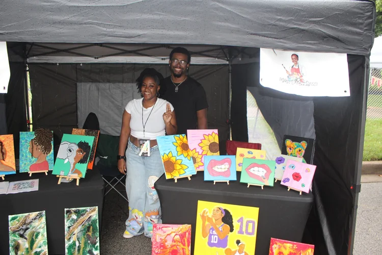 Bright paintings and two smiling booth participants. 18th & Vine Arts Festival 2026.