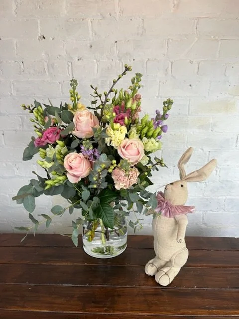 A romantic, wreath decorated with pink, purple and red flowers, dried foliage, cinnamon sticks, and hanging velvet ribbons at the base, hung on white wall.