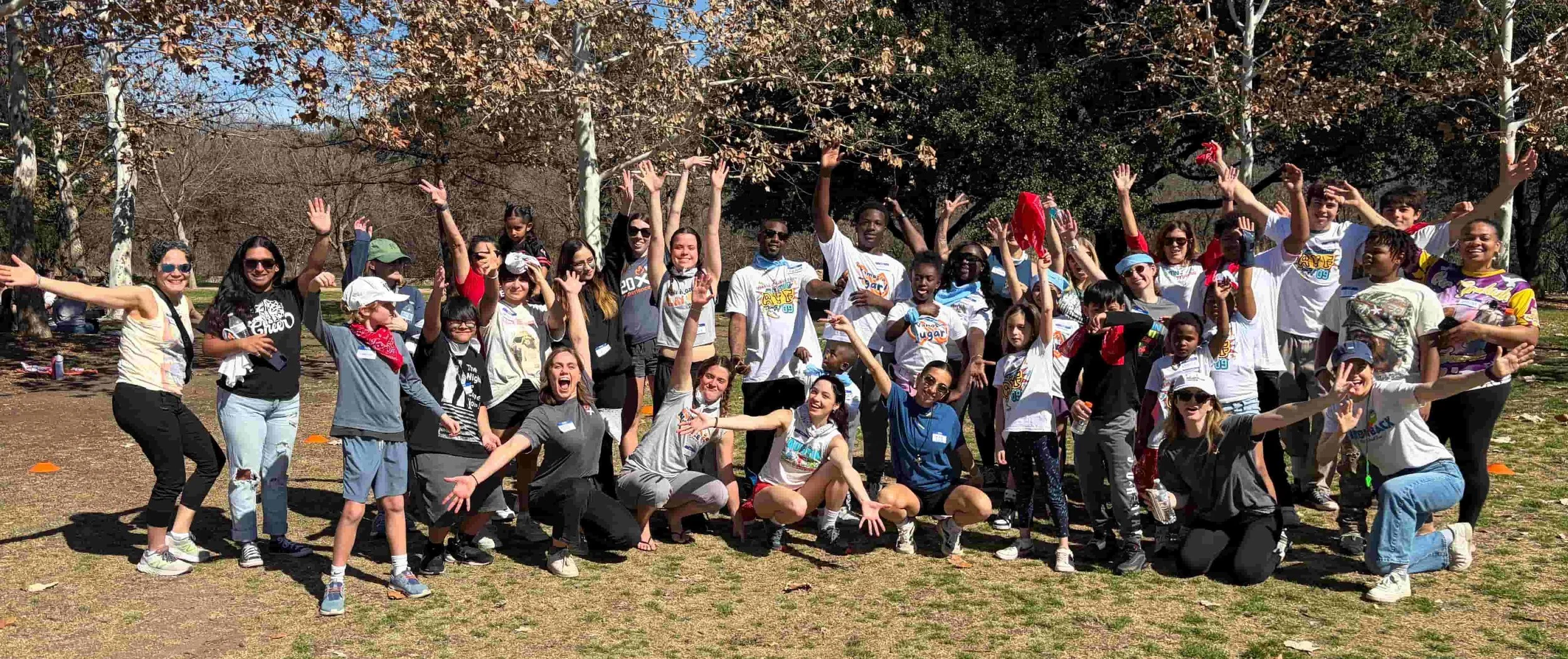 Campers and Throwback volunteers cheer together with arms raised in a group photo outdoors at a field day for Experience Camps