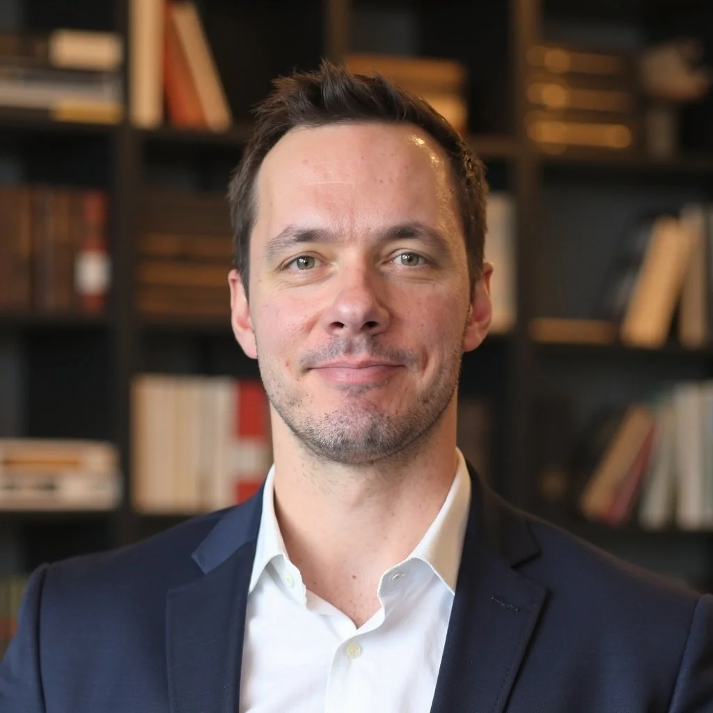 A smiling man wearing glasses and a casual t-shirt, standing against a plain white background.