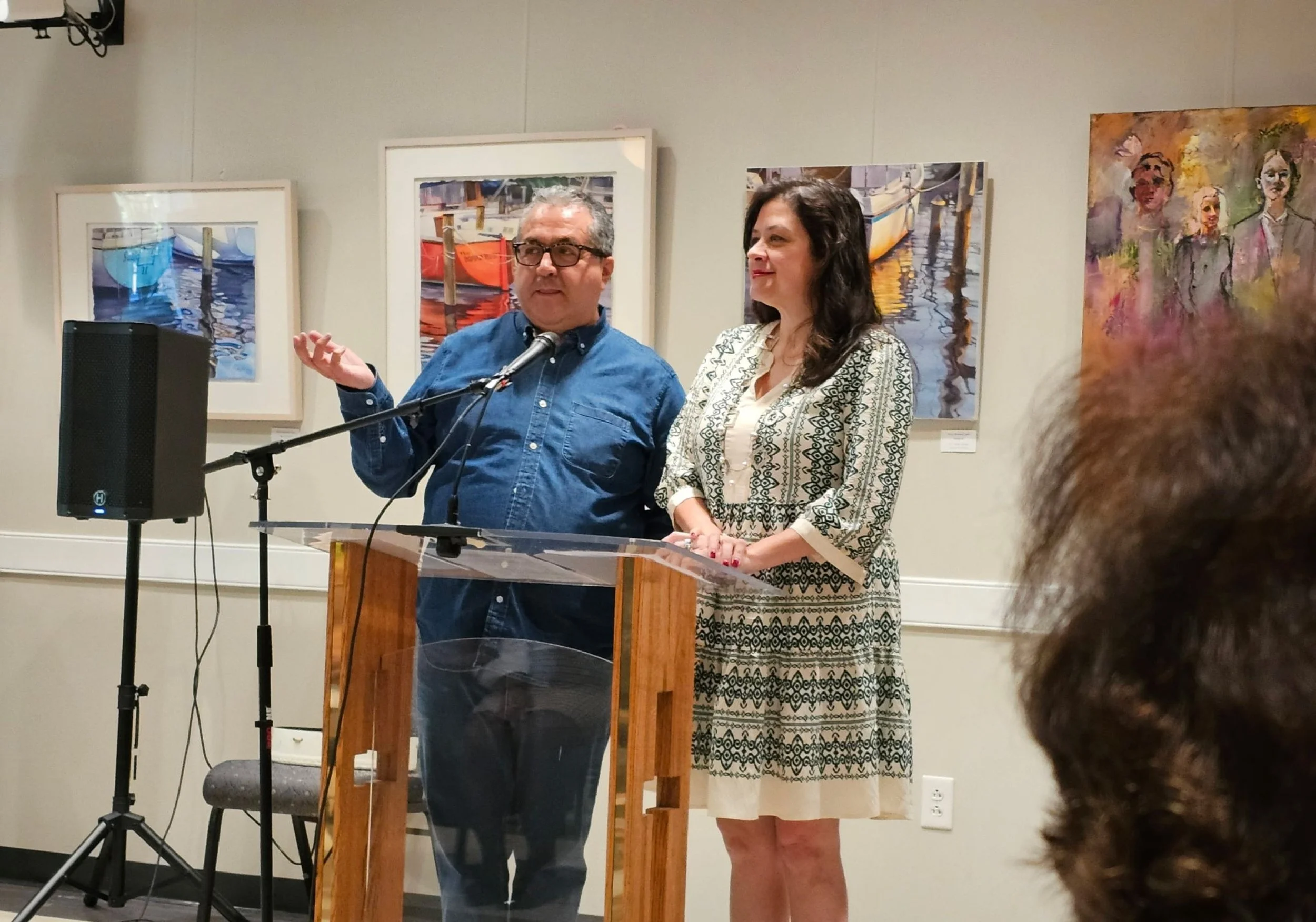 Dos personas hablando en una presentación o evento en un museo, con obras de arte pintadas en las paredes detrás de ellos.