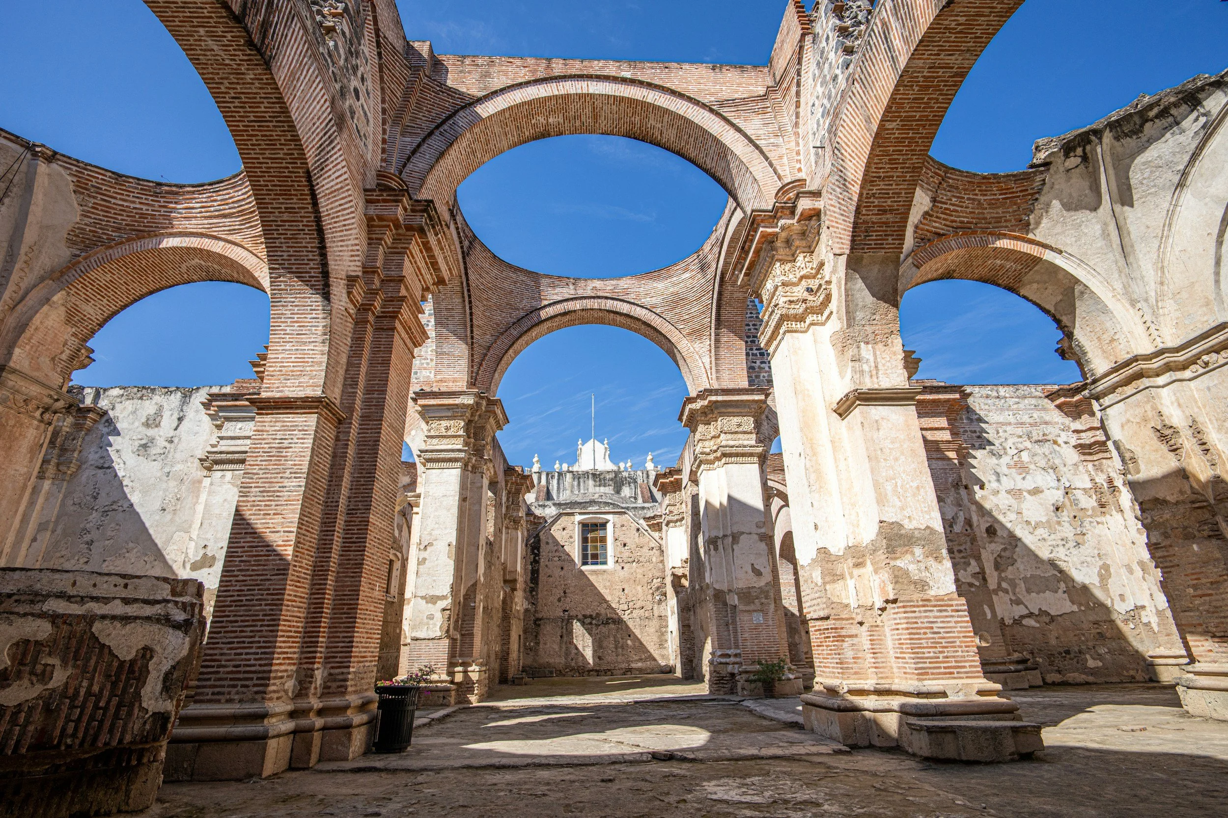 The remains of an ancient brick and stone ruin, with arches and columns, under a clear blue sky.
