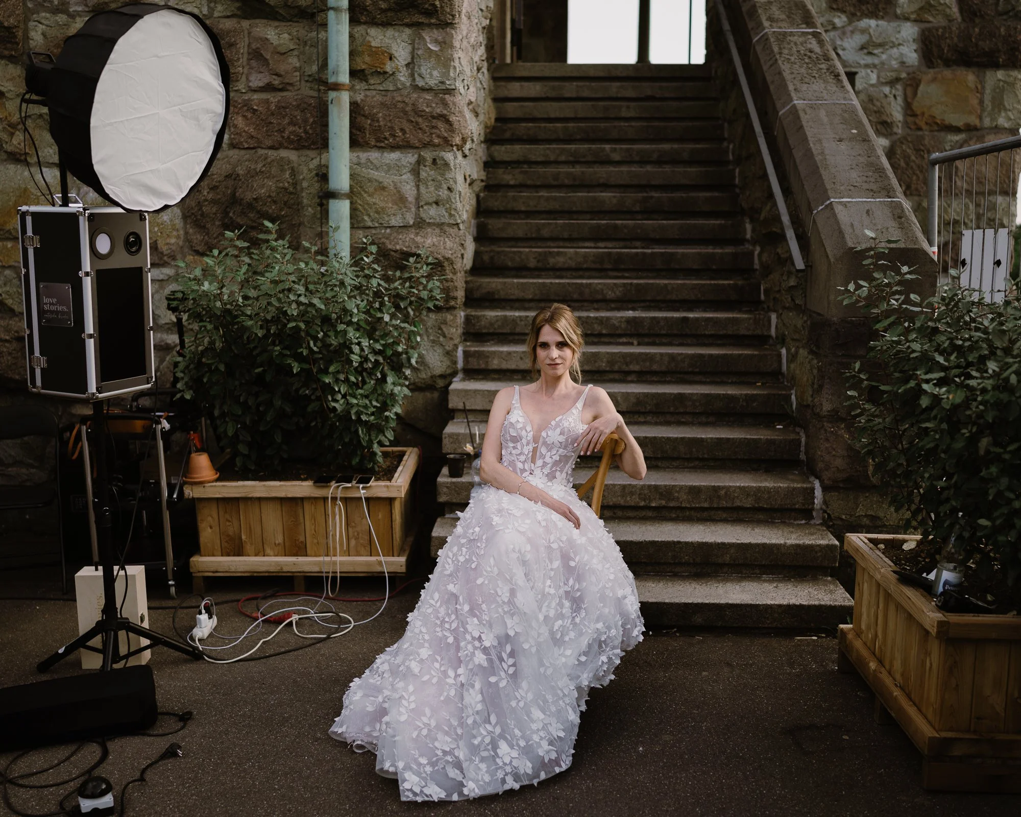 Braut sitzt auf einem Stuhl und mit Blitz links von ihr und Treppe hinter sich